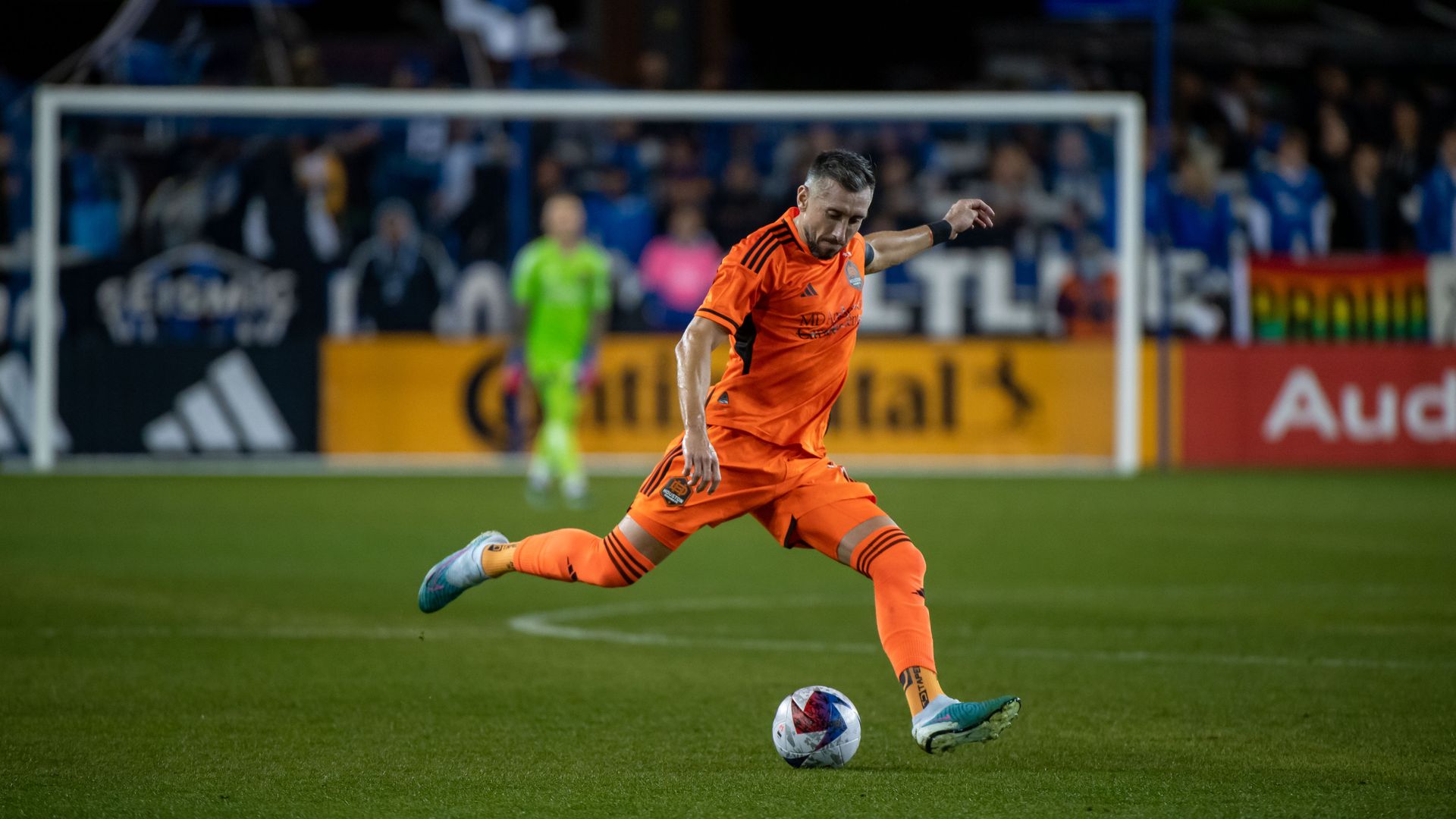 The Dynamo's Hector Herrera, wearing an orange professional soccer uniform, sets up a kick