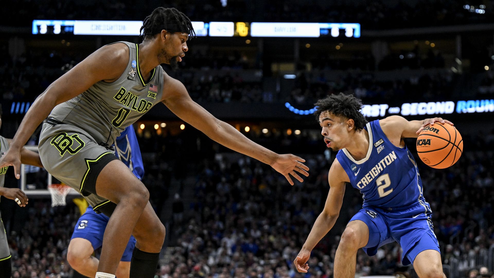 Two basketball players face one another while one holds onto a bright orange ball. 