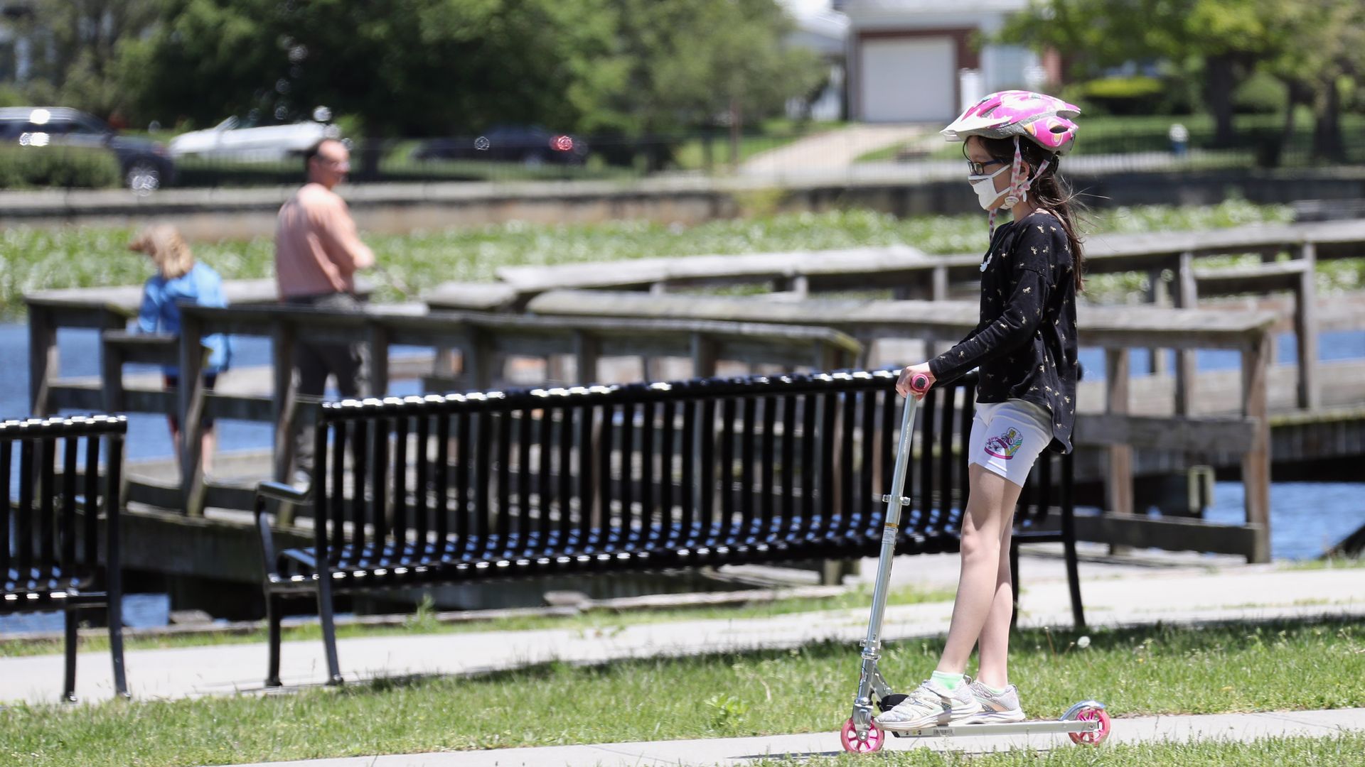 A child with a mask is seen on a scooter. 