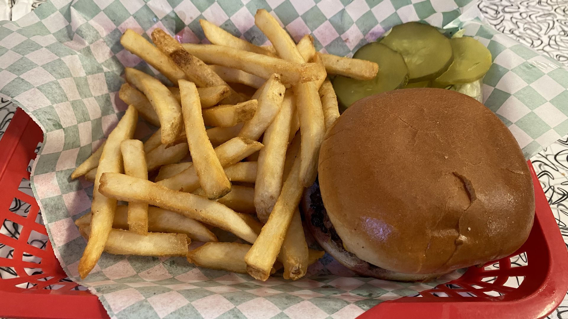 A hamburger, French fries and pickle slices in a red plastic tray.