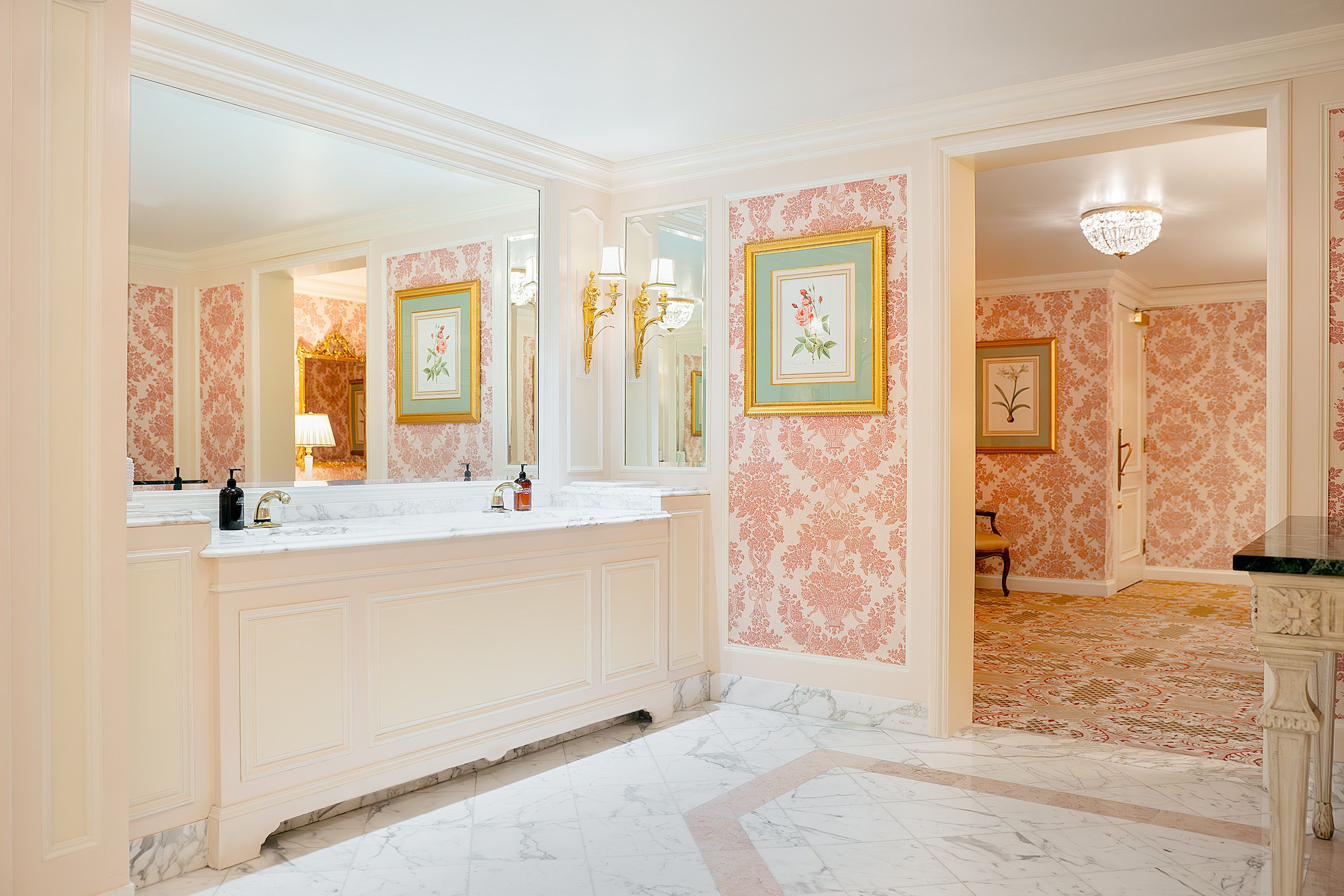 A restroom with pink wallpaper and chandeliers. 