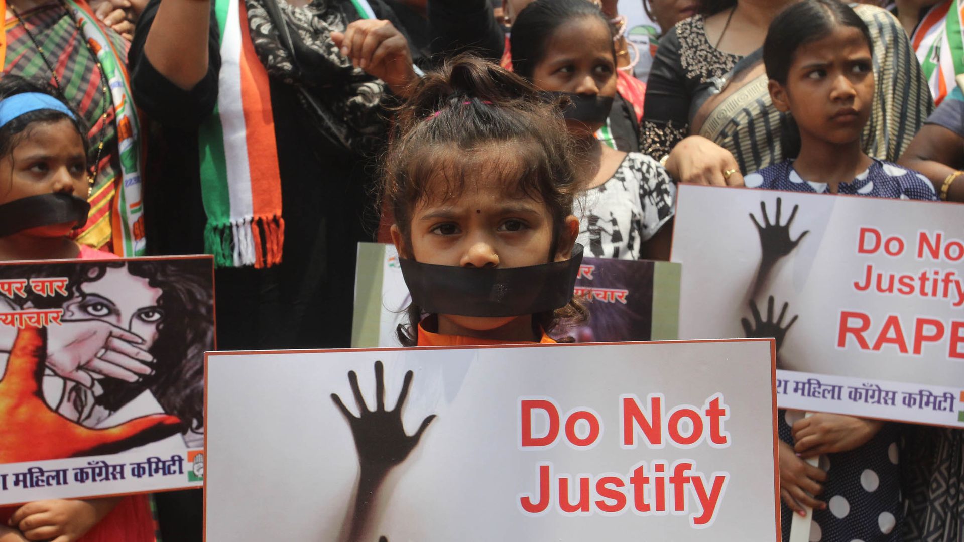 A young girl holds a sign that reads "Do not justify rape."