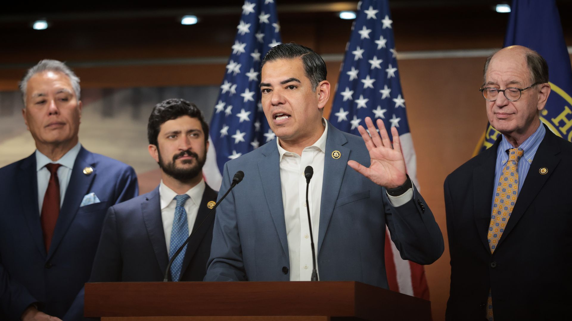 Rep. Robert Garcia wearing a gray suit and speaking at a press conference with colleagues.