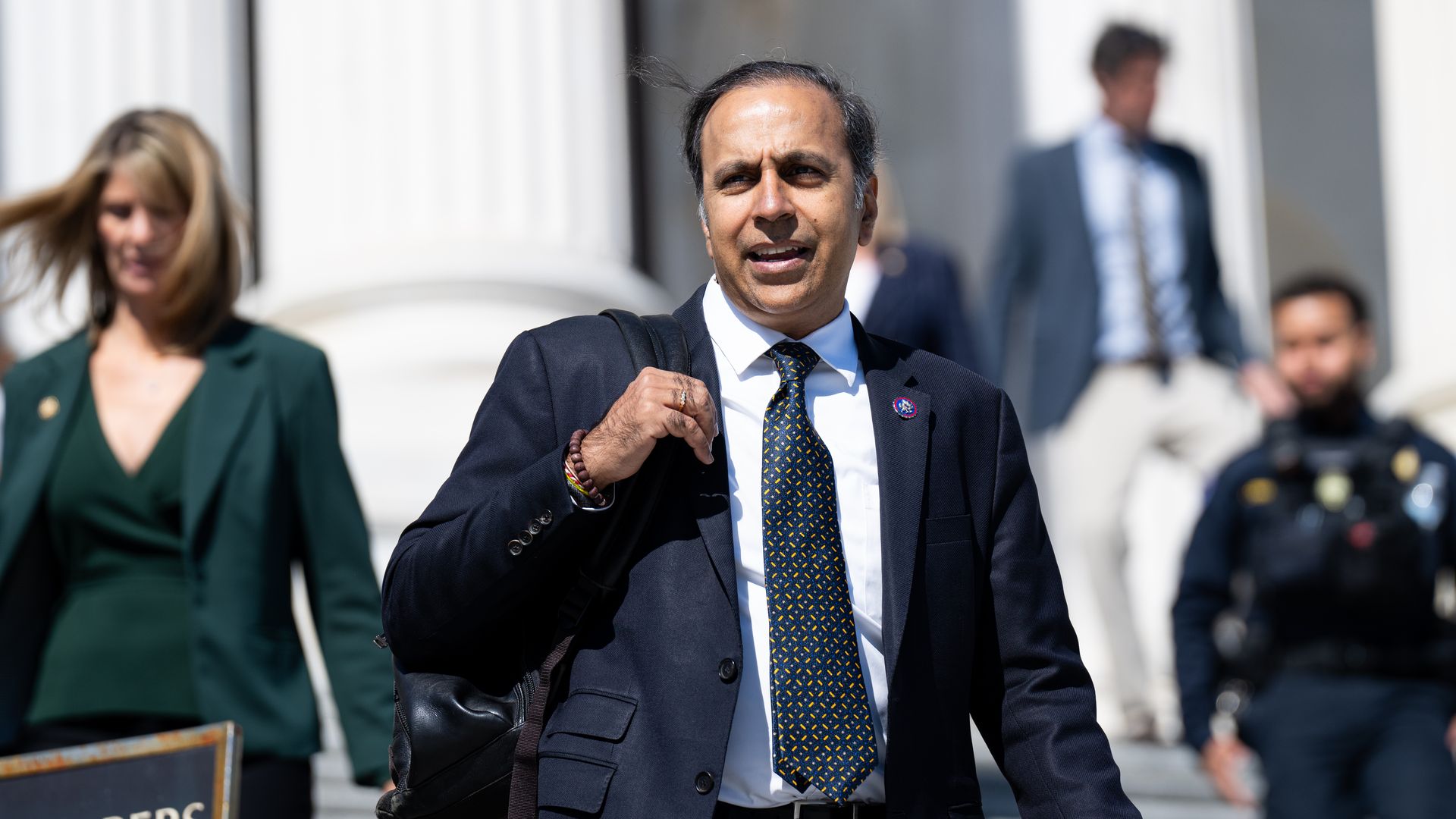 Photo of a man in a suit walking down steps in front of a big rotunda building. 