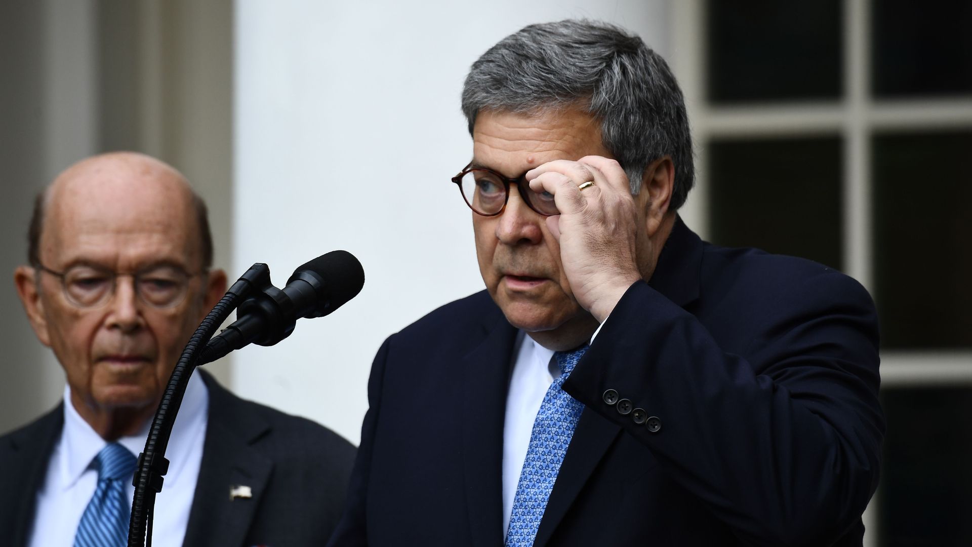 In this image, Barr and Ross stand outside in front of a microphone. Barr adjusts his glasses.