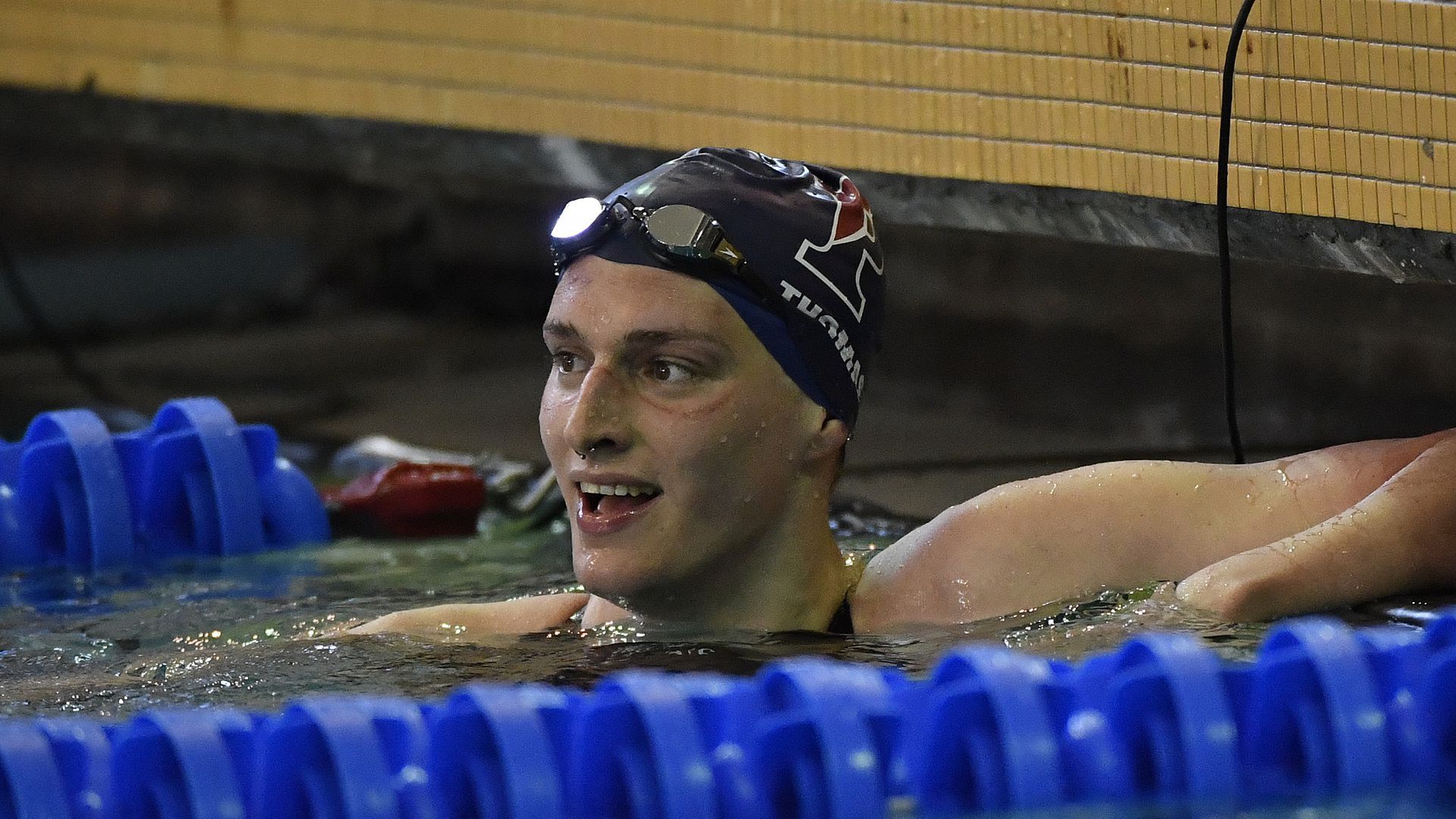 Lia Thomas smiles in the pool while wearing a Penn swimming cap and goggles on her forehead.