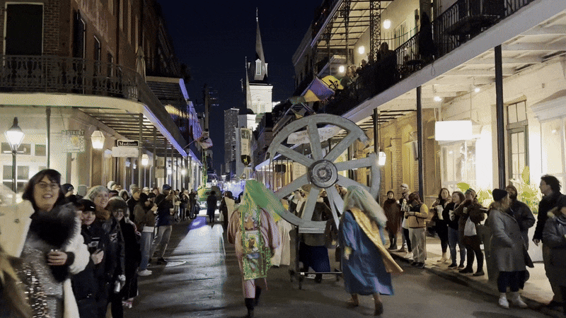Parade marchers walk along Chartres Street toward the St. Louis Cathedral as onlookers watch.