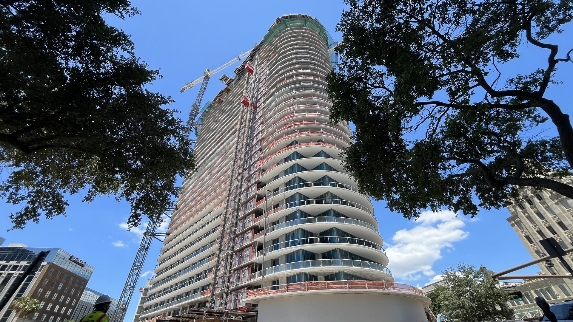 The rounded front of an under-construction skyscraper framed by two trees. 