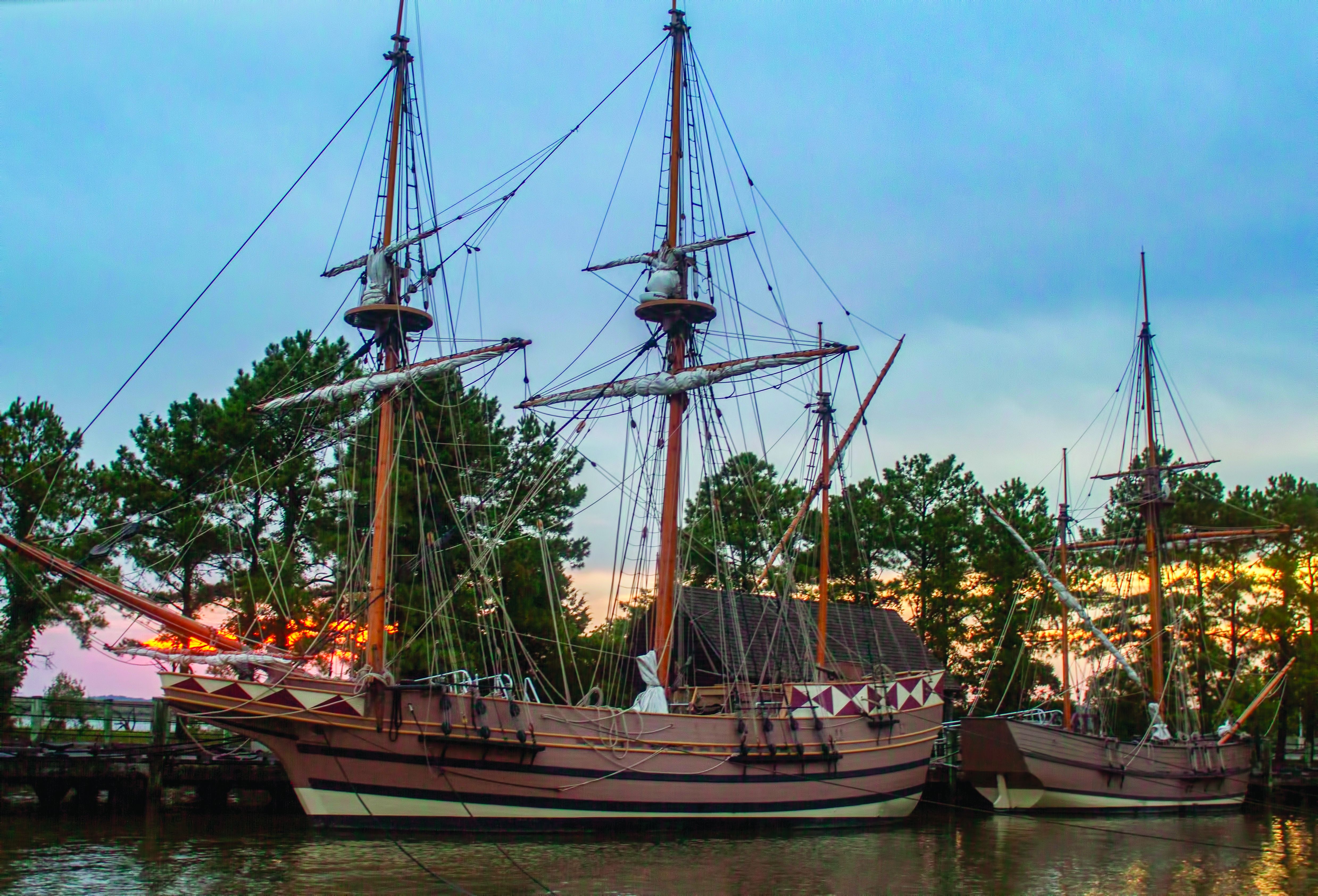 Two tall ships docked during sunset at the Jamestown settlement.