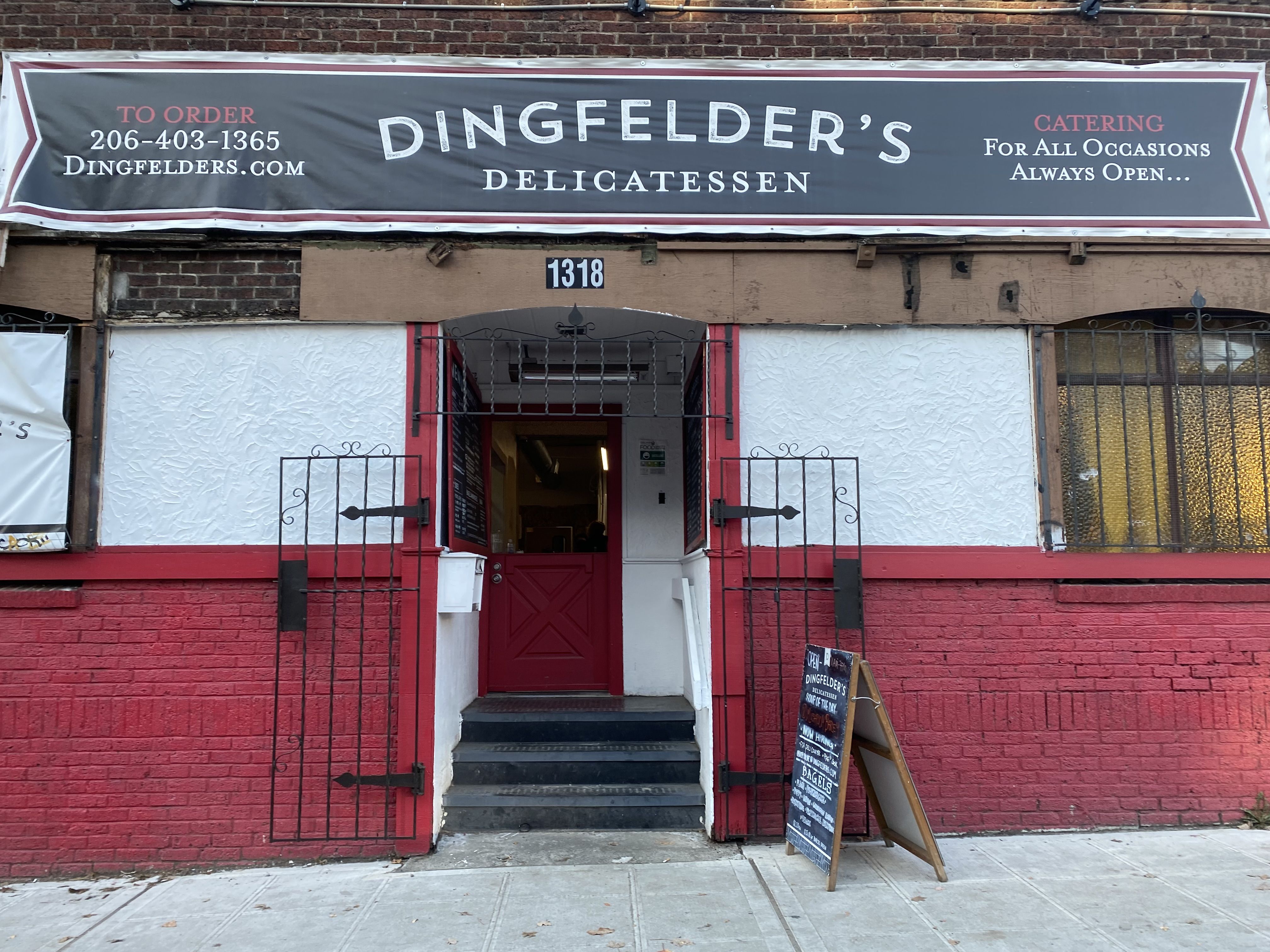 A view of a storefront with a sign that says "Dingfelder's" overhead, and a sandwich board on the sidewalk.