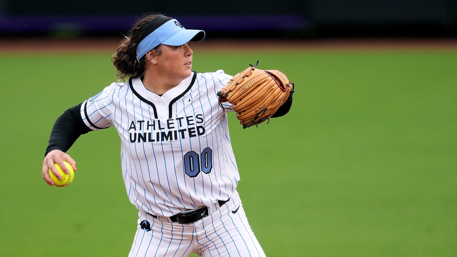 A person in a light blue visor and softball uniform prepares to throw a softball