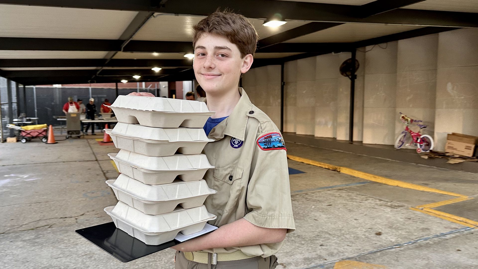 Photo shows a Boy Scout carrying several compostable boxes of fish dinners.