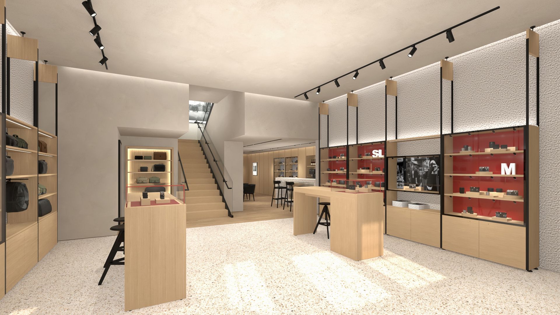 Modern boutique interior with light wood shelves, red display cases on the right, track lighting, speckled terrazzo floor, central wooden tables, and a staircase to a mezzanine.