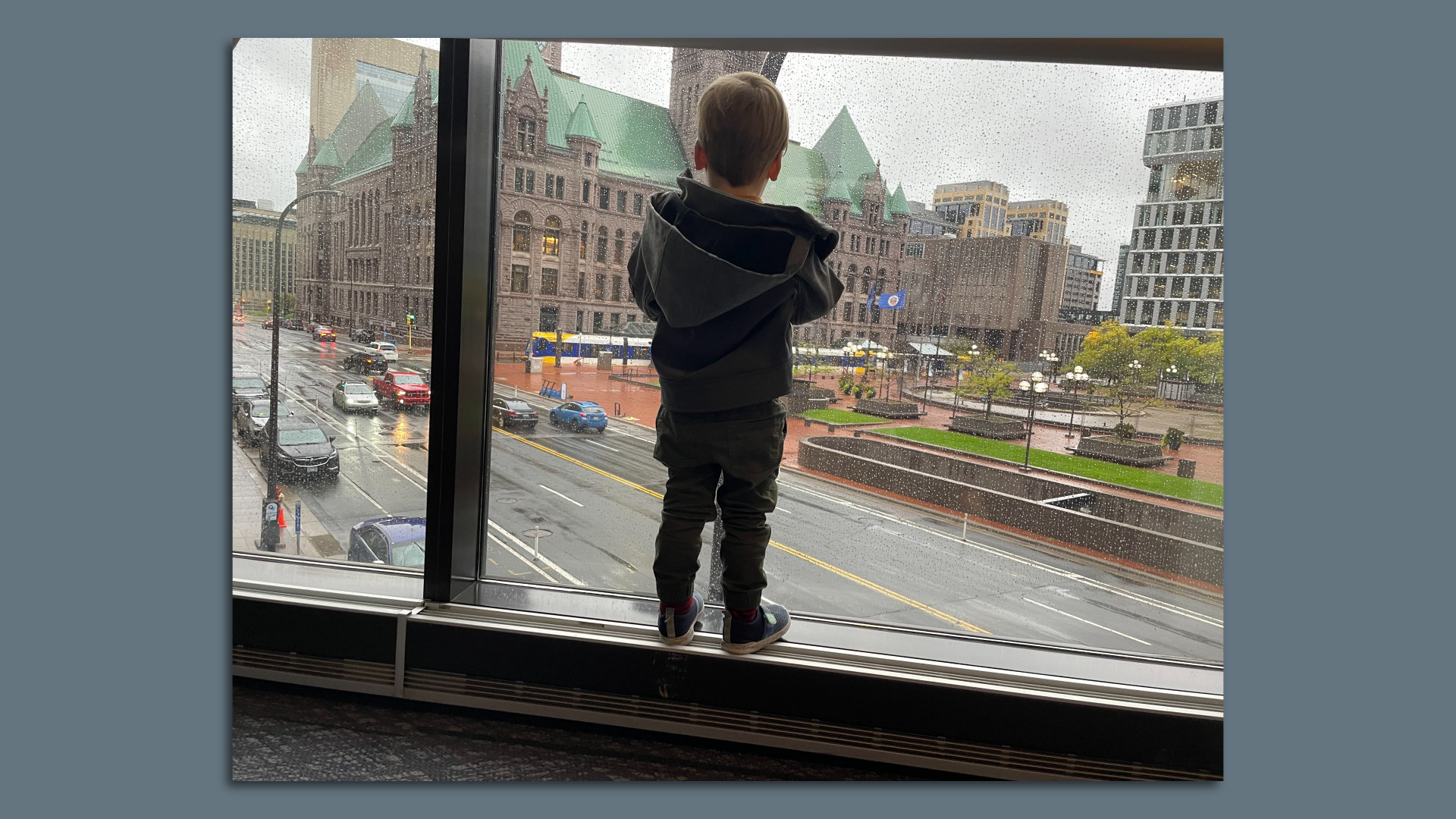 A little boy stands at awindow looking over a street