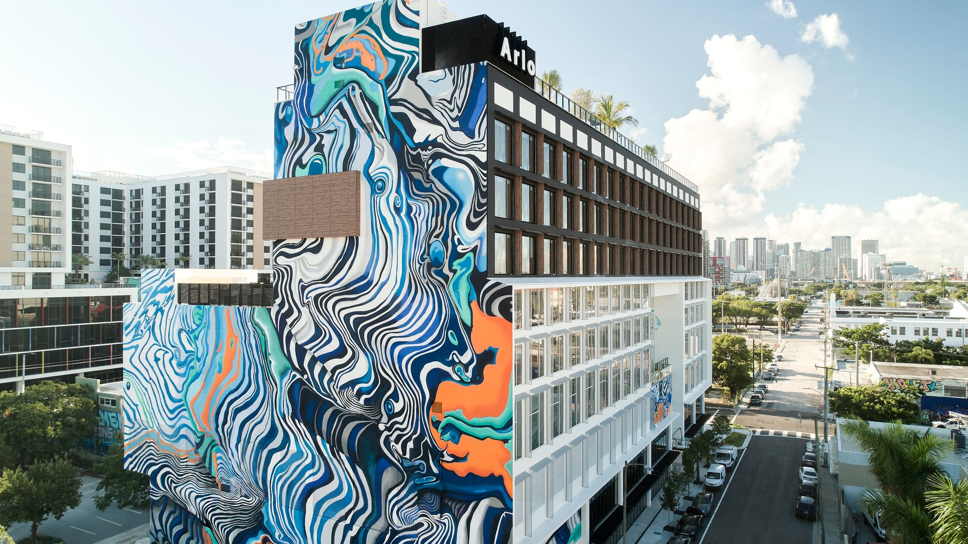The exterior of the new Arlo hotel, with a bright, abstract mural appearing like ink in water, painted on its side.
