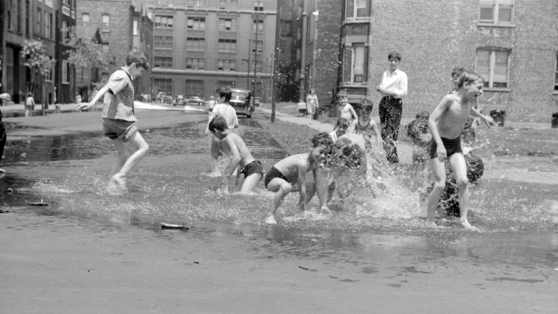 Black and white photo of kids playing in water in the street in 1947