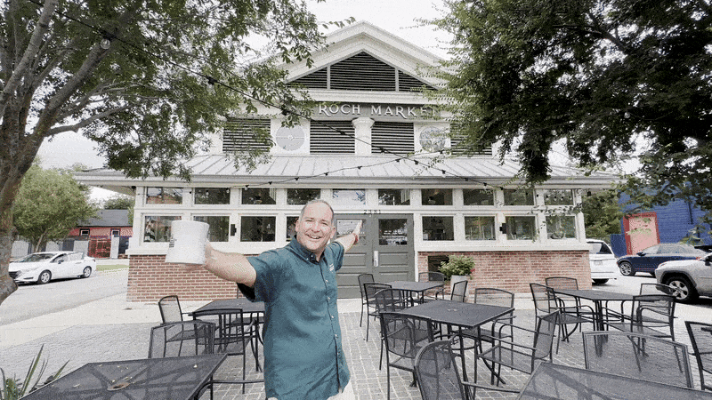 Image shows Kevin Pedeaux gesturing with a coffee cup in front of St. Roch Market.