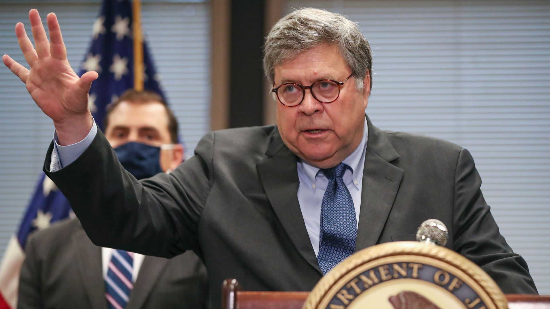 Barr stands with a raised hand behind a podium