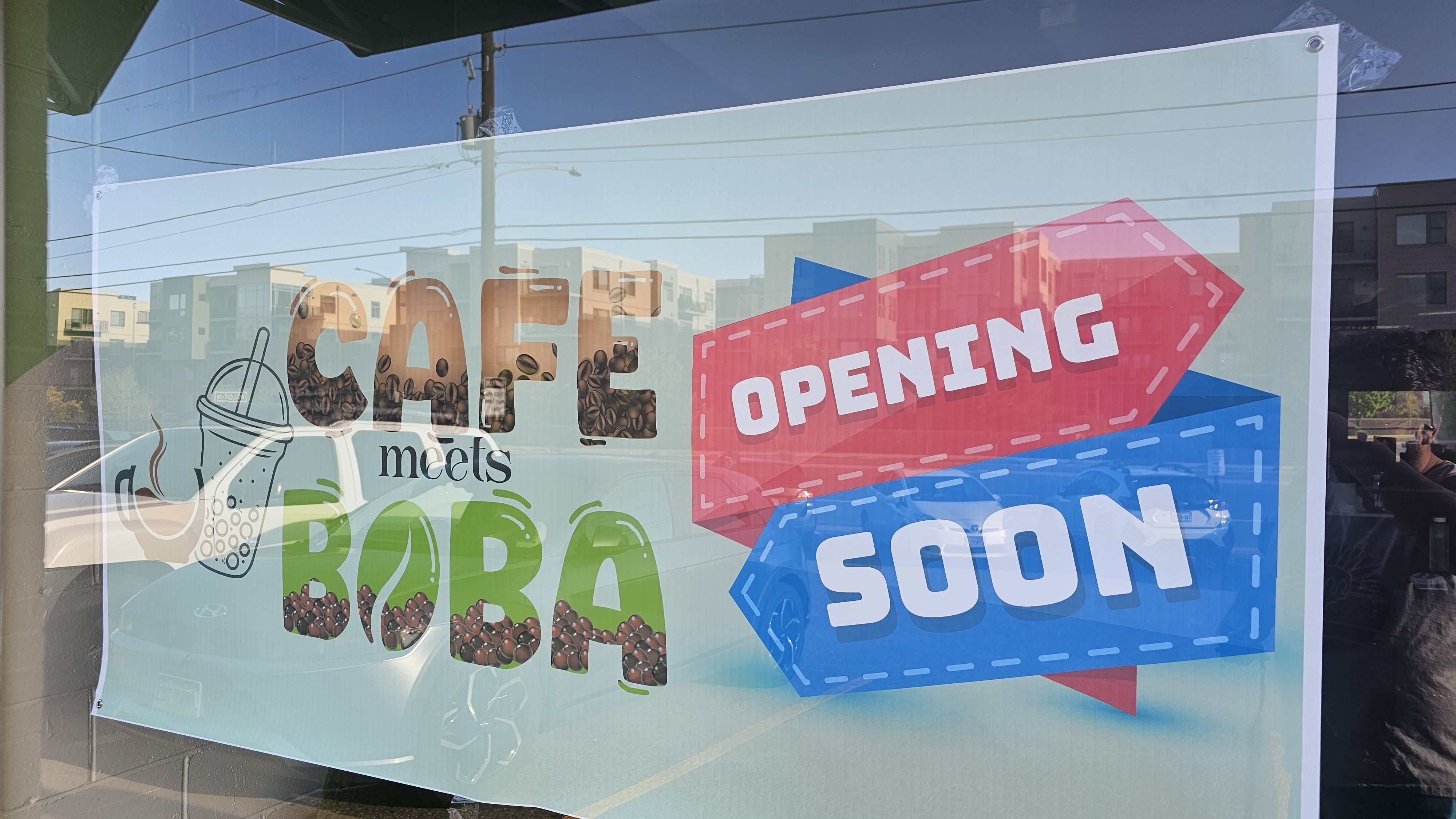 Storefront poster reads "COFFEE meets BOBA" with coffee beans; a pink arrow sign reads "OPENING" and a blue panel says "SOON." Glass reflection shows street and power lines.