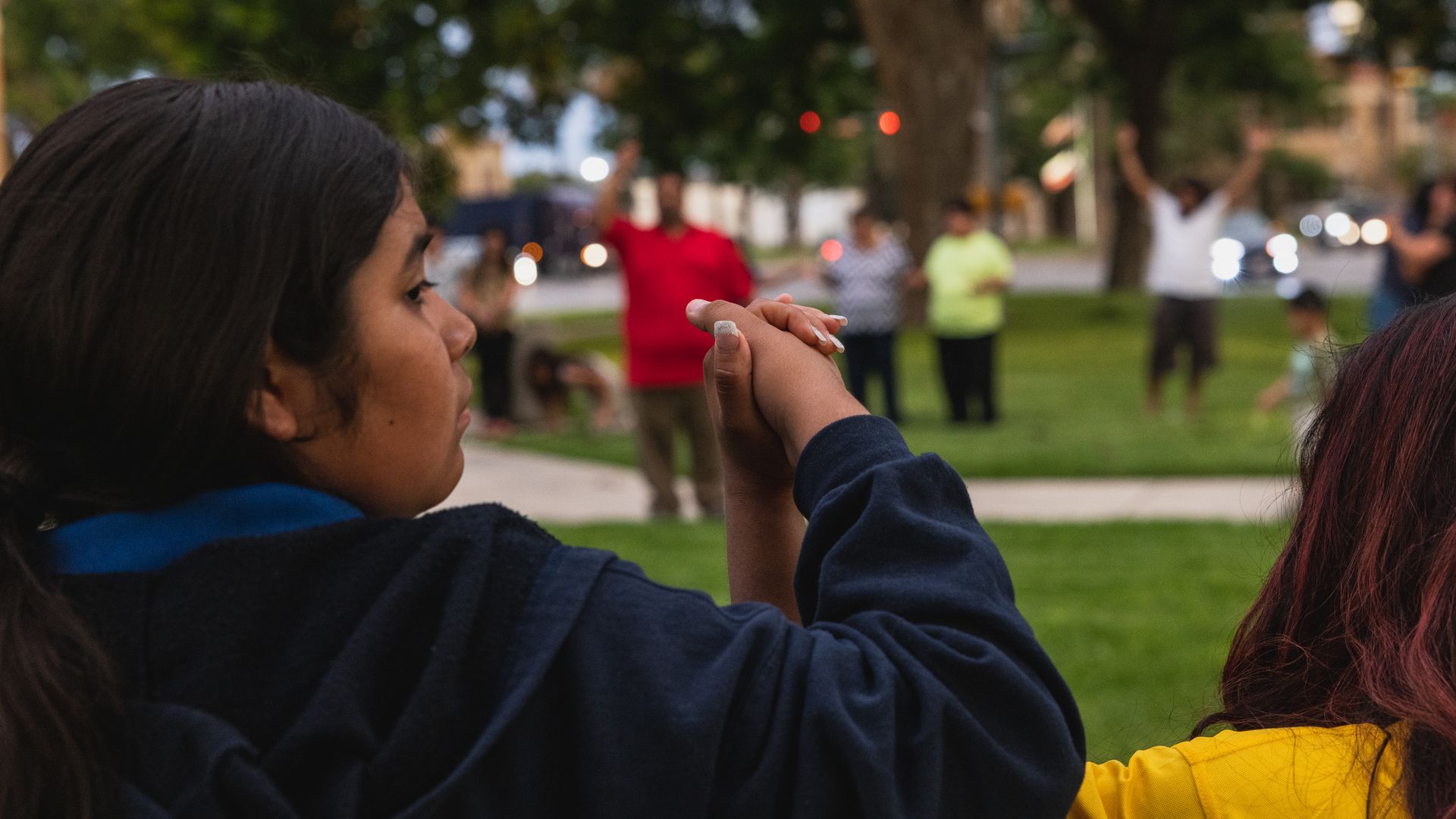A young girl is holding hands with someone in a prayer circle at a vigil for shooting victims in Uvalde, Texas