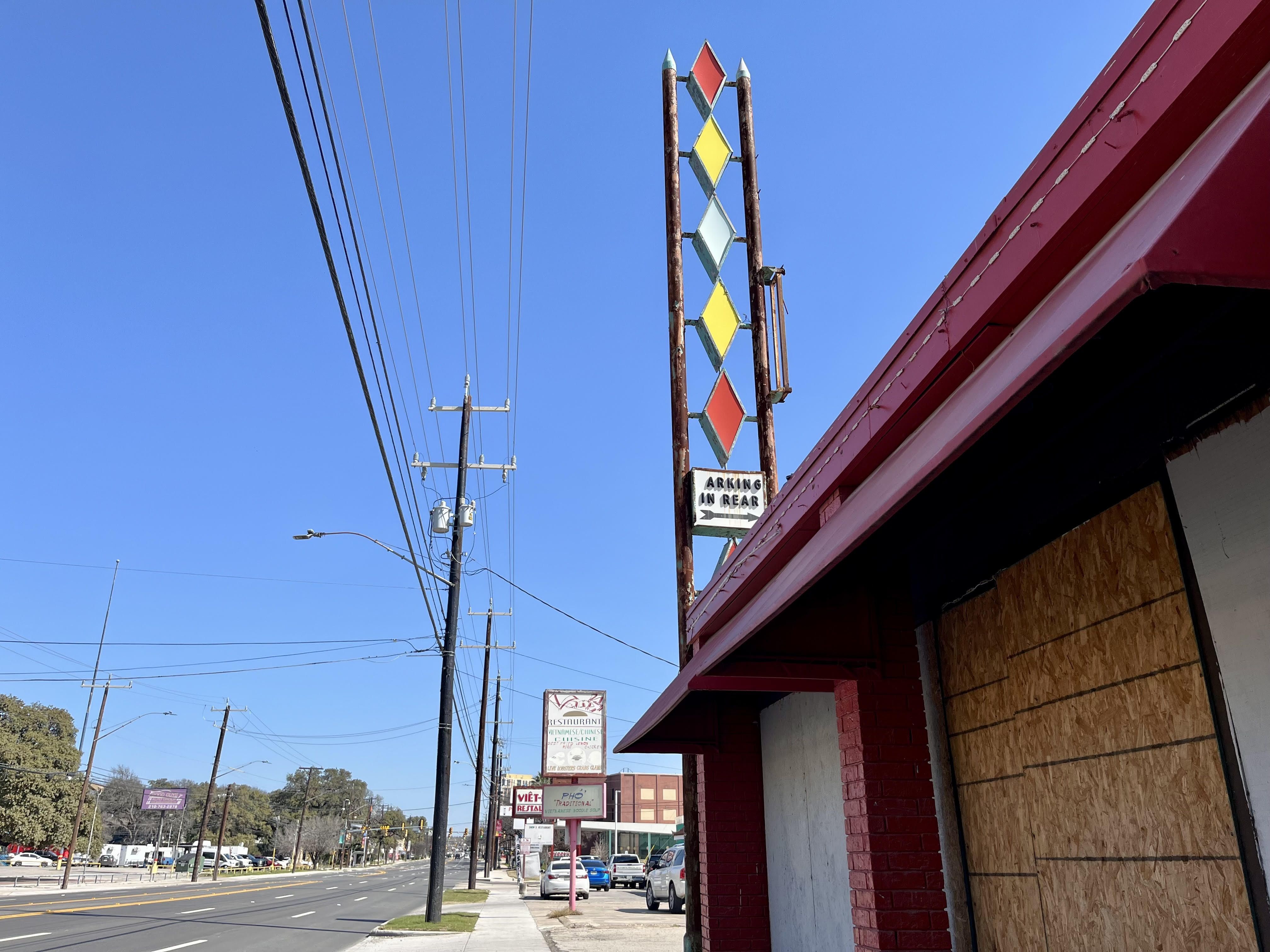 A boarded-up former business on Broadway with a colorful parking sign above it.