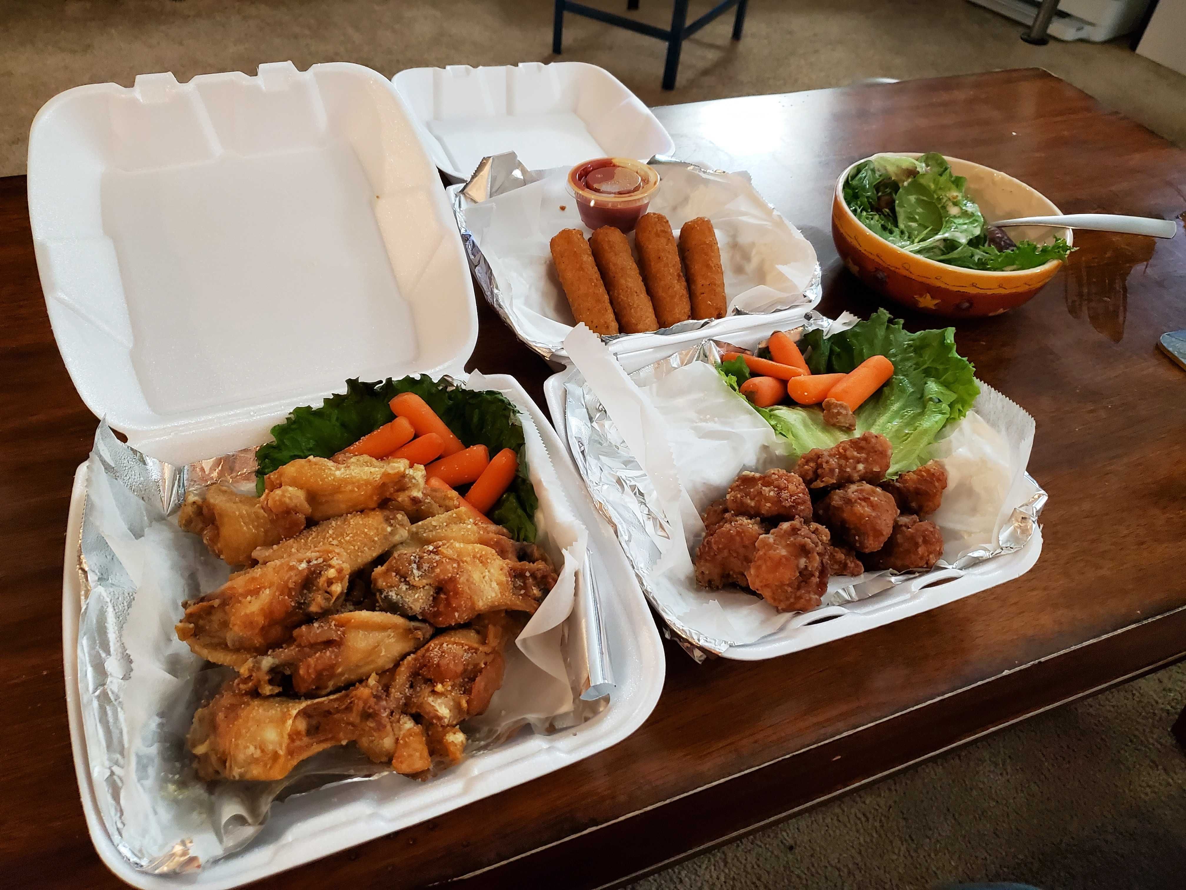 To-go containers full of wings, mozzarella sticks and a salad