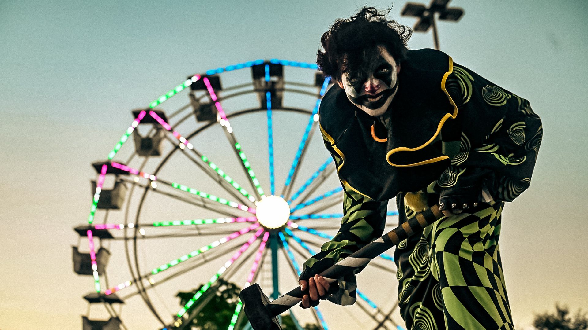 A scary clown with a ferris wheel in the background.