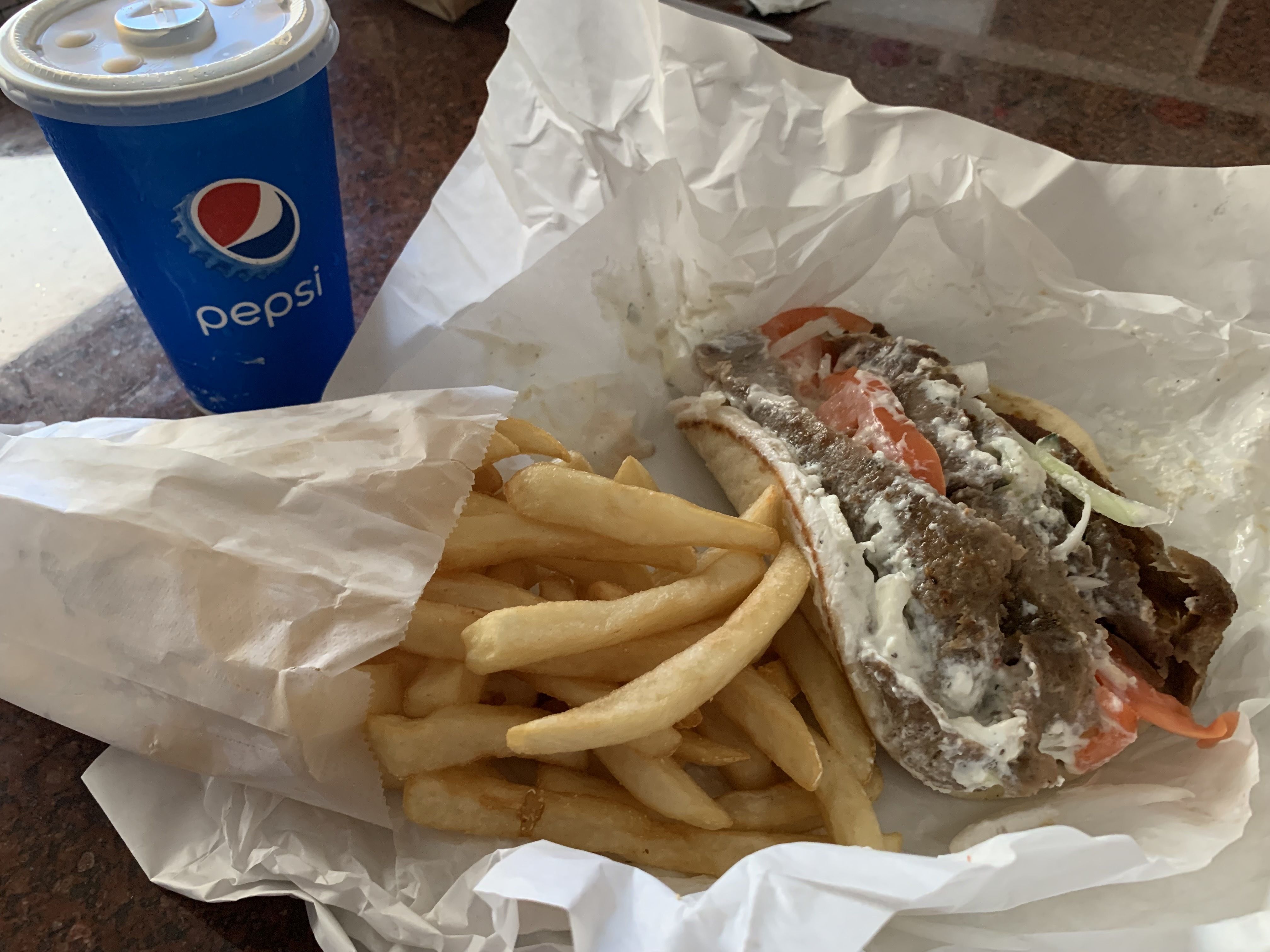 Photo of a gyros sandwich with fries and a drink. 