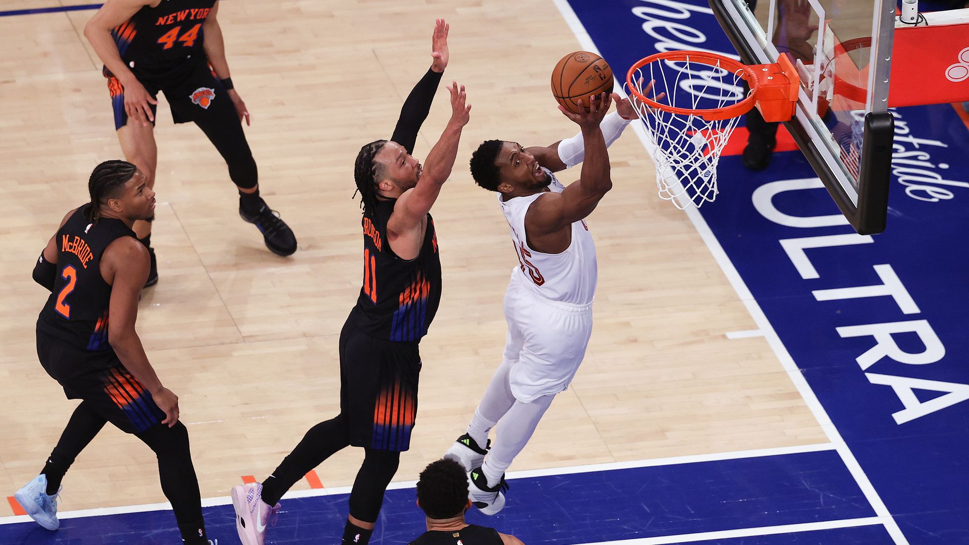 Donovan Mitchell in white jersey goes for layup with multiple Knicks in black jerseys swarming to block