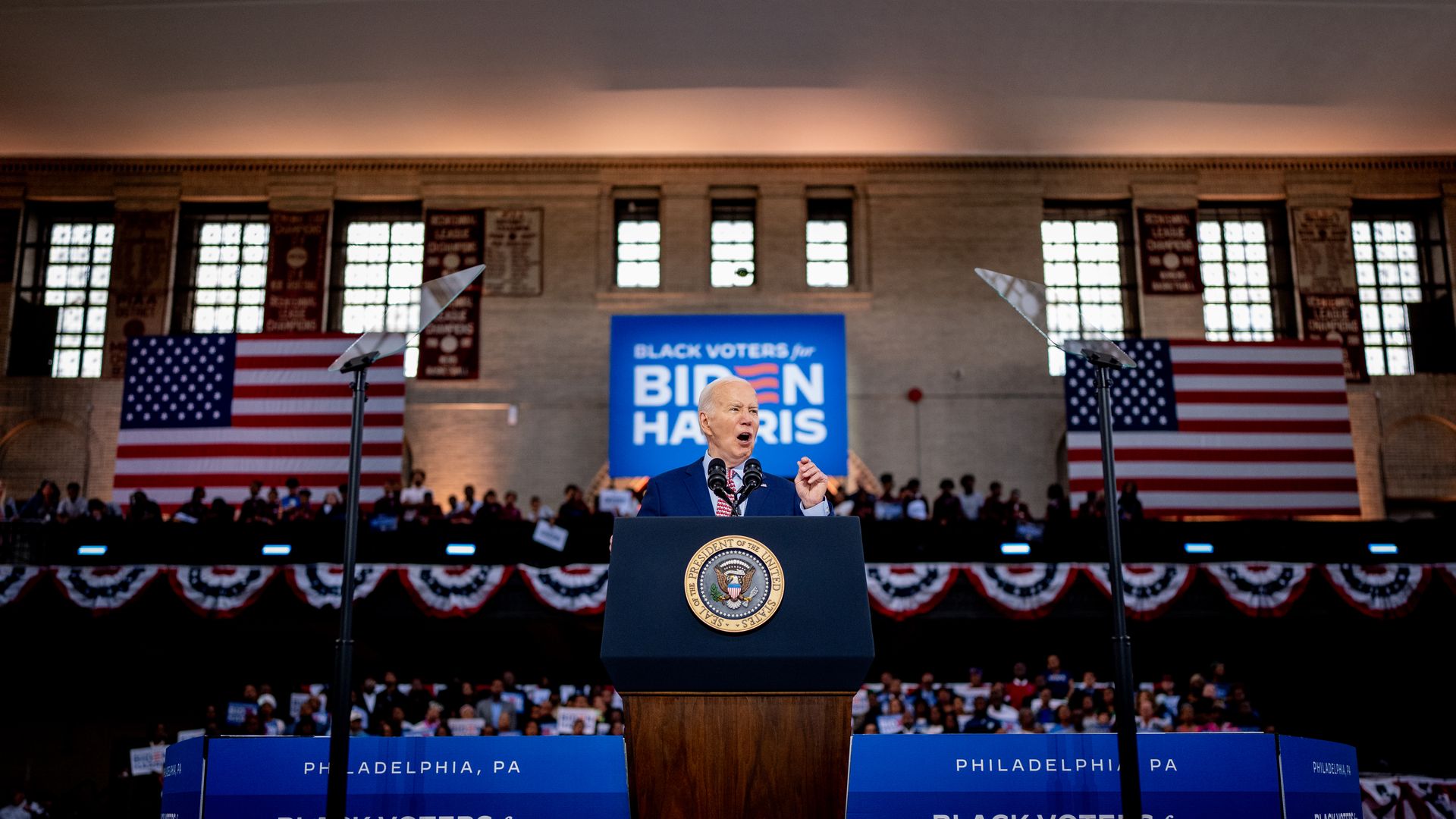 Biden campaigning before a lectern and two American flags over his shoulders