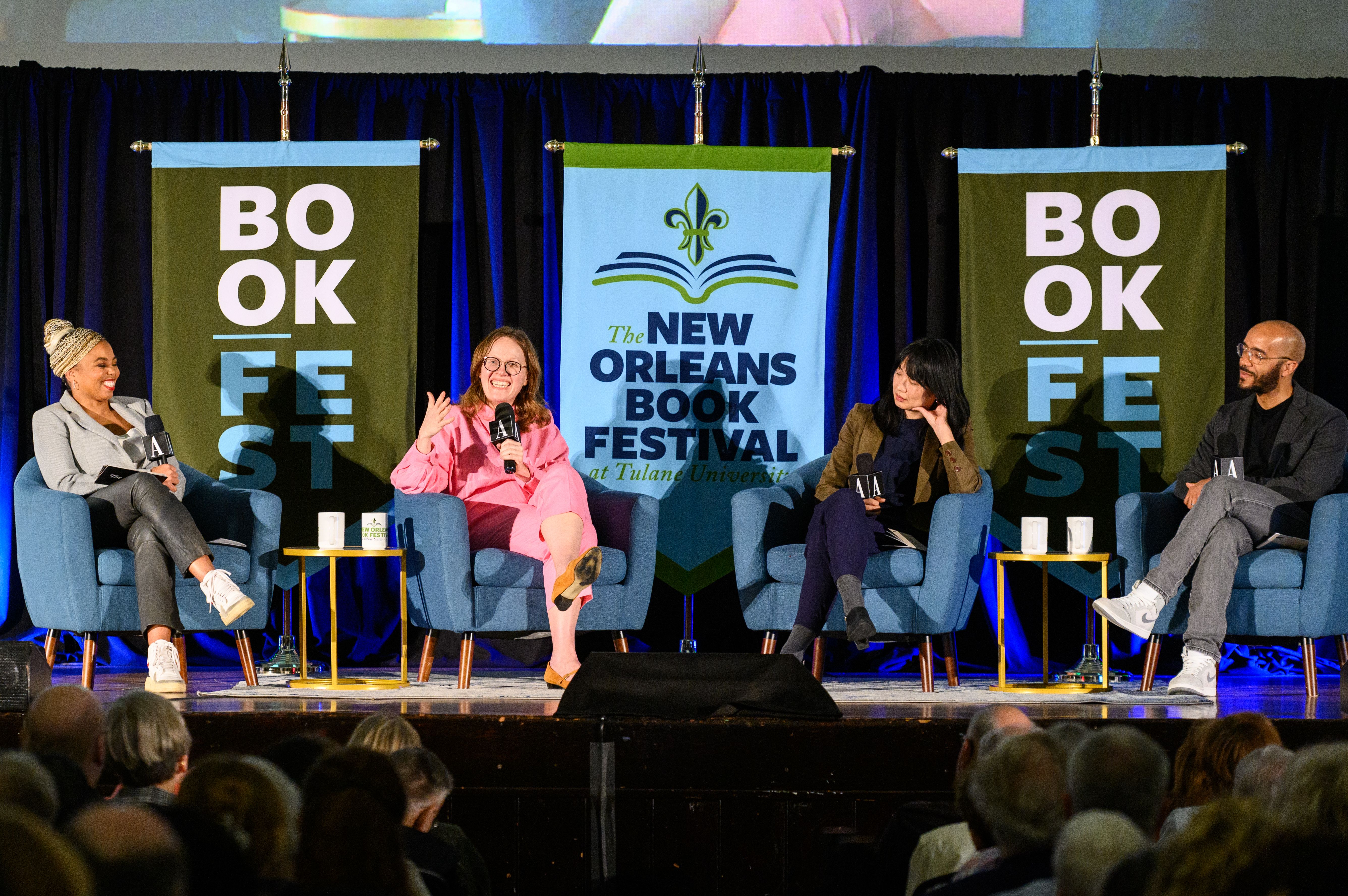 Four people sit in armchairs on a stage. Behind them are banners that say New Orleans Book Festival.