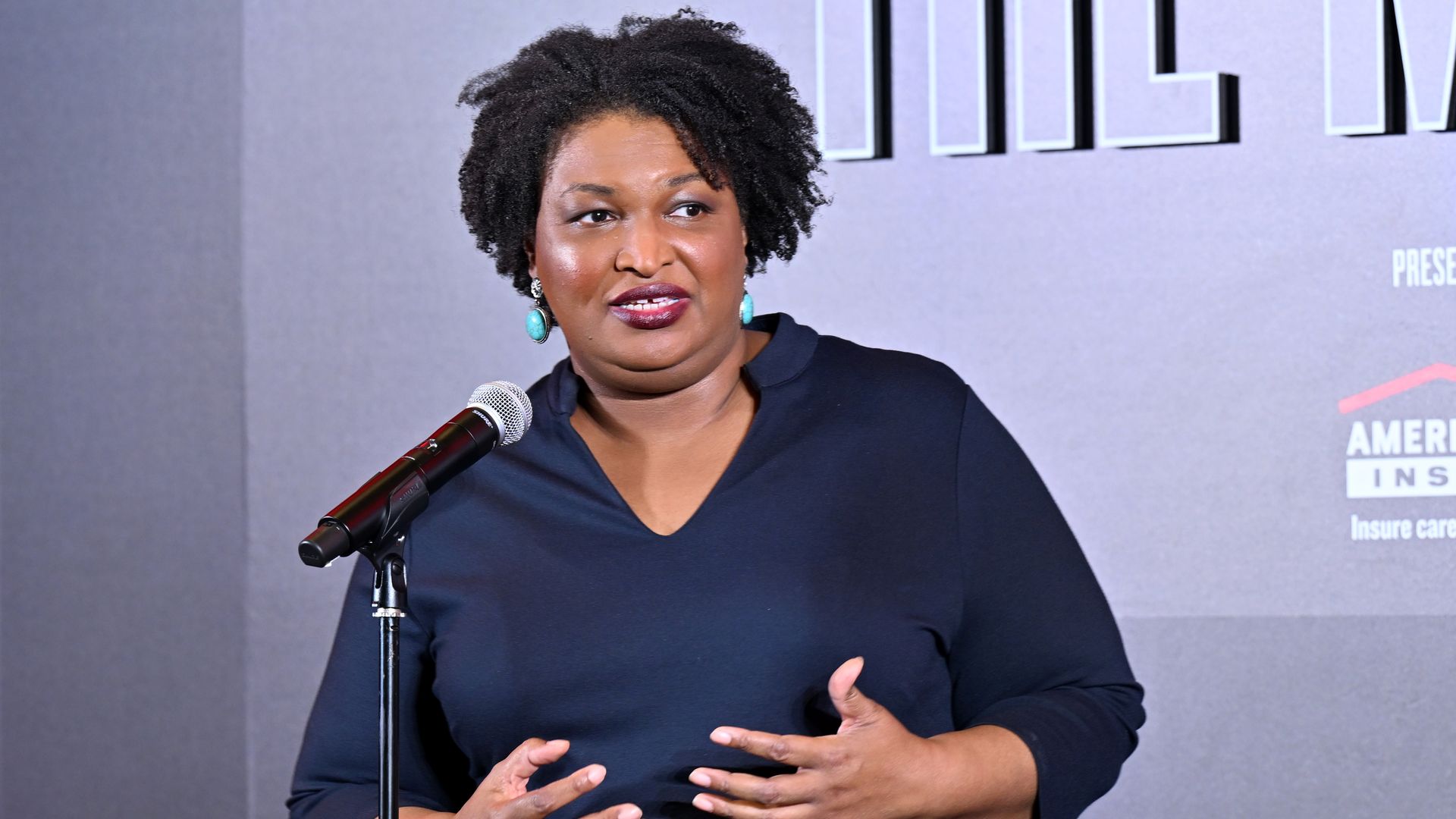 Stacey Abrams, wearing a dark blue blouse, speaks behind a microphone.