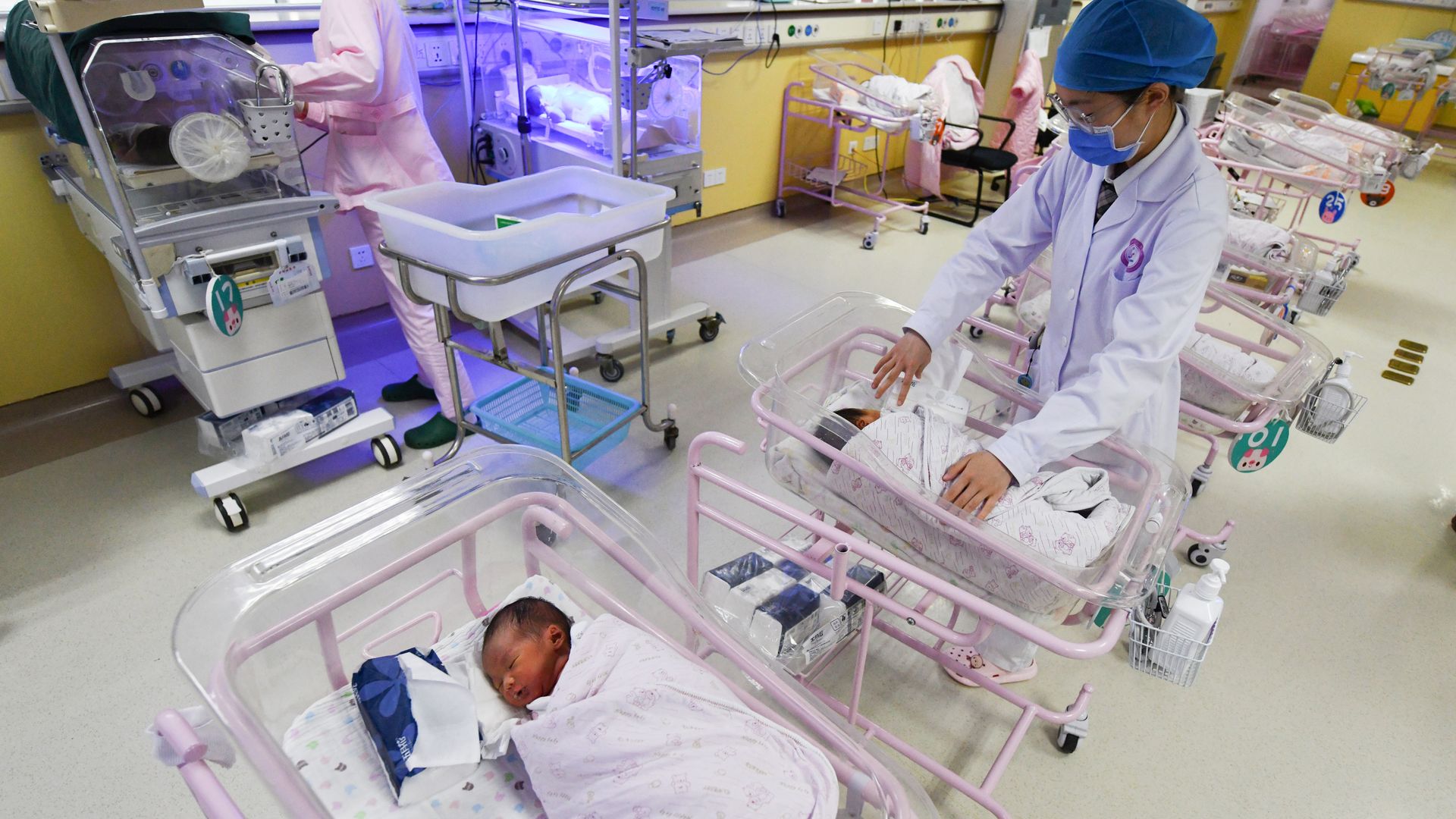 Picture of a hospital in China with newborns in cribs and two hospital workers 