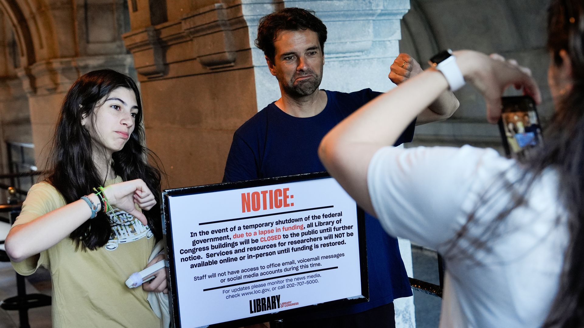 People take photos with a sign announcing the Library of Congress is closed to the public.