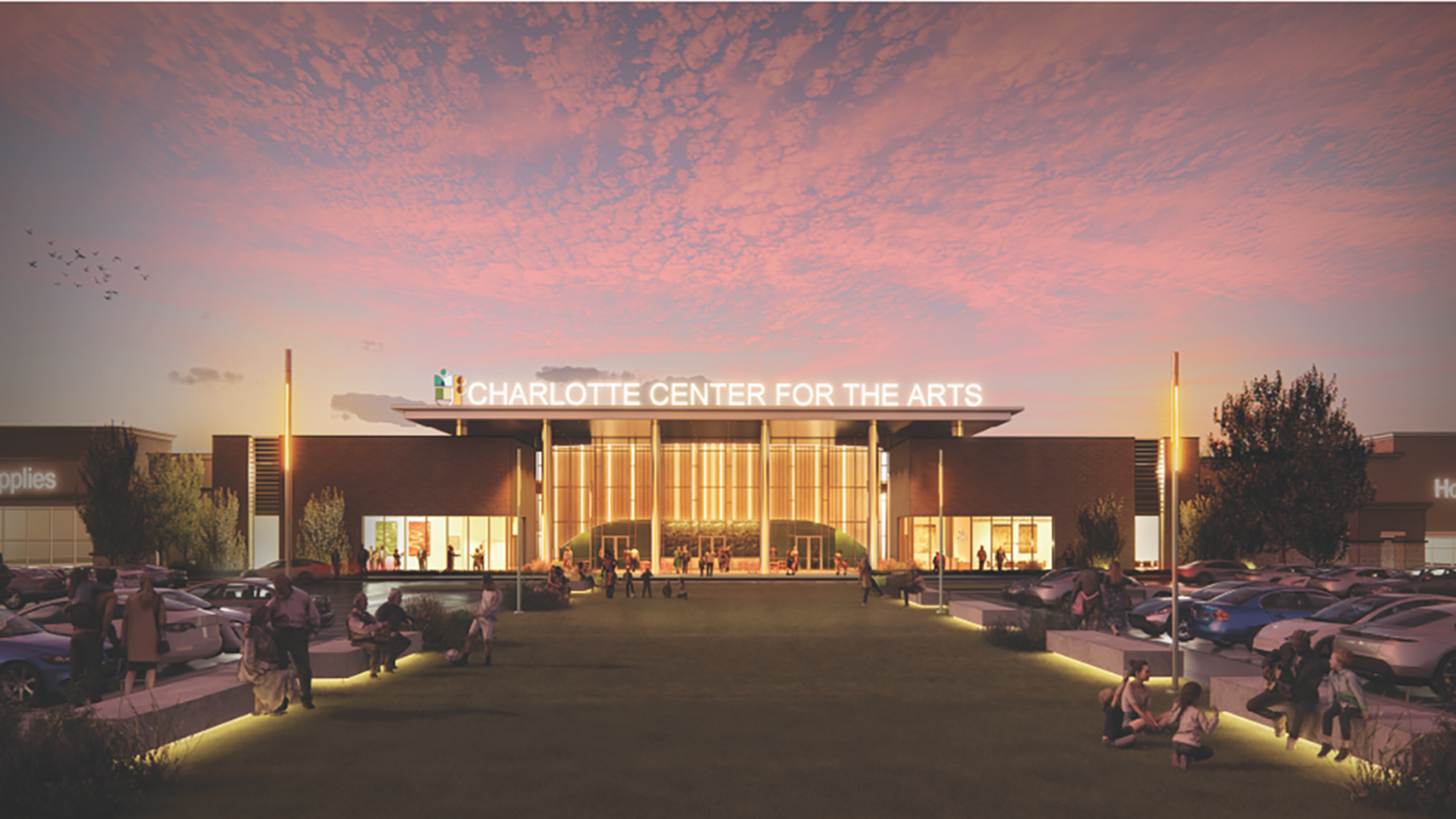 Sunset sky over the Charlotte Center for the Arts, a modern brick building with a bright glass entrance, people gathering outside, parked cars, trees, and illuminated walkways.