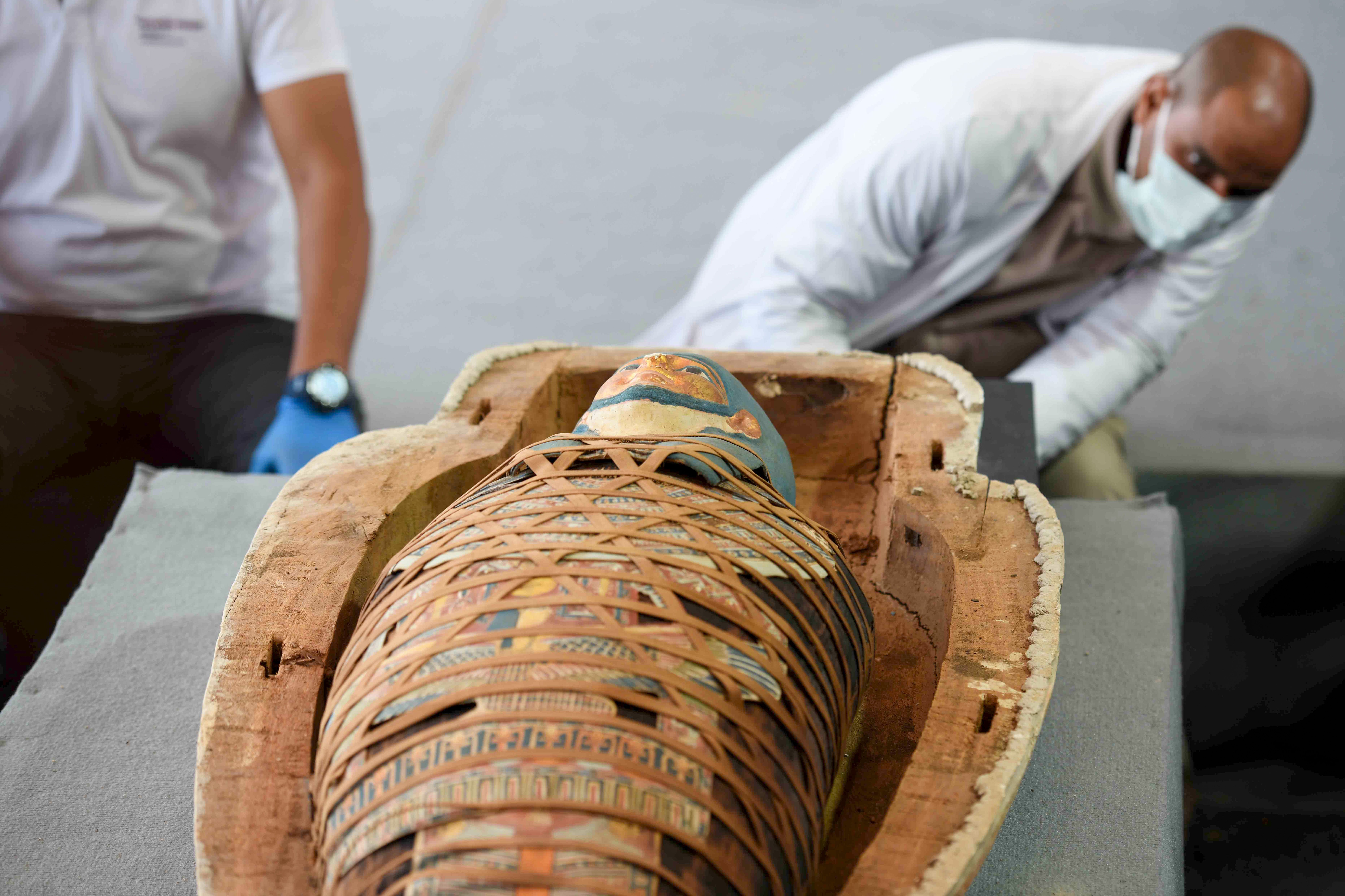 Archaeologists inspect a mummy, wrapped in a burial shroud adorned with brightly coloured hieroglyphic pictorials