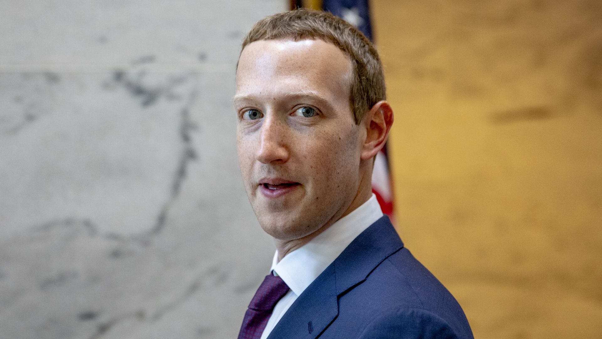 In this image, Zuckerberg's profile is turned away from the camera as he faces it head-on. He's wearing a suit