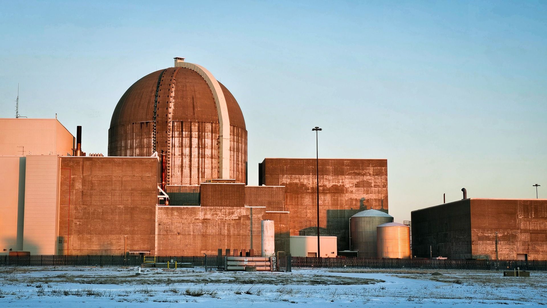 The large industrial Wolf Creek nuclear power plant with a domed reactor building, additional rectangular structures, and metal silos, set against a clear blue sky with snow-covered ground.