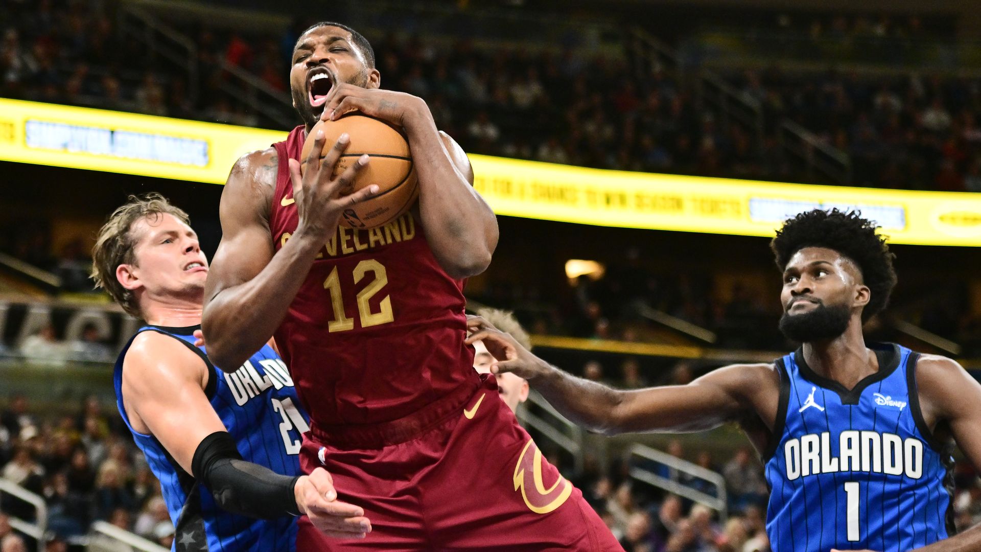 The Cavs' Tristan Thompson collects a rebound between two blue-shirted Orlando Magic players.