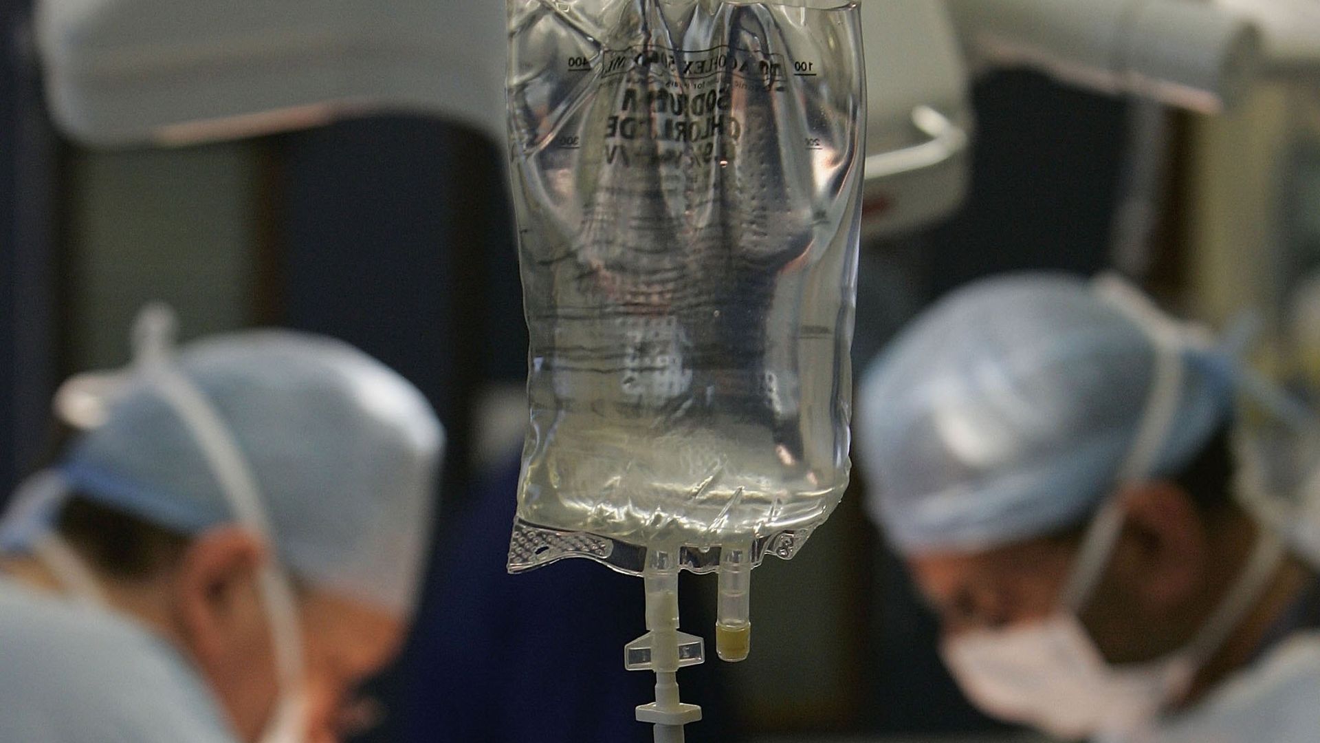 An IV bag hangs as surgeons conduct an operation.