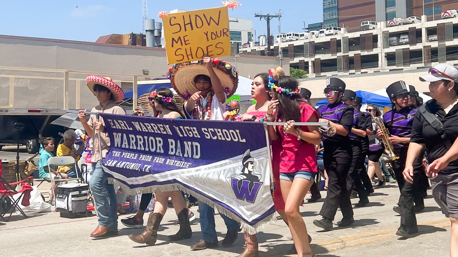 A high school band marches while holding banners and signs.
