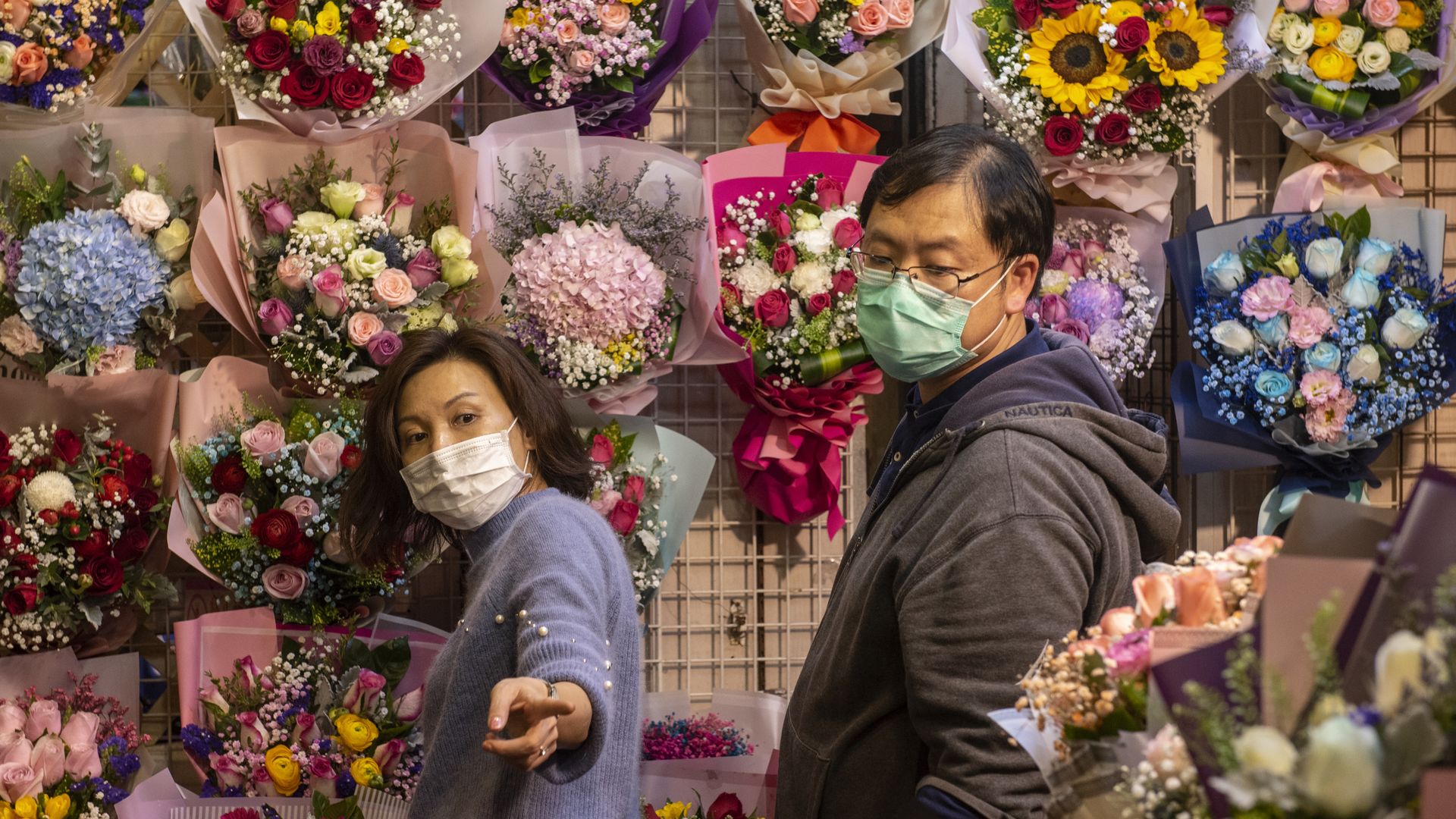 In this image, a woman and man wearing protective face masks browse flowers 