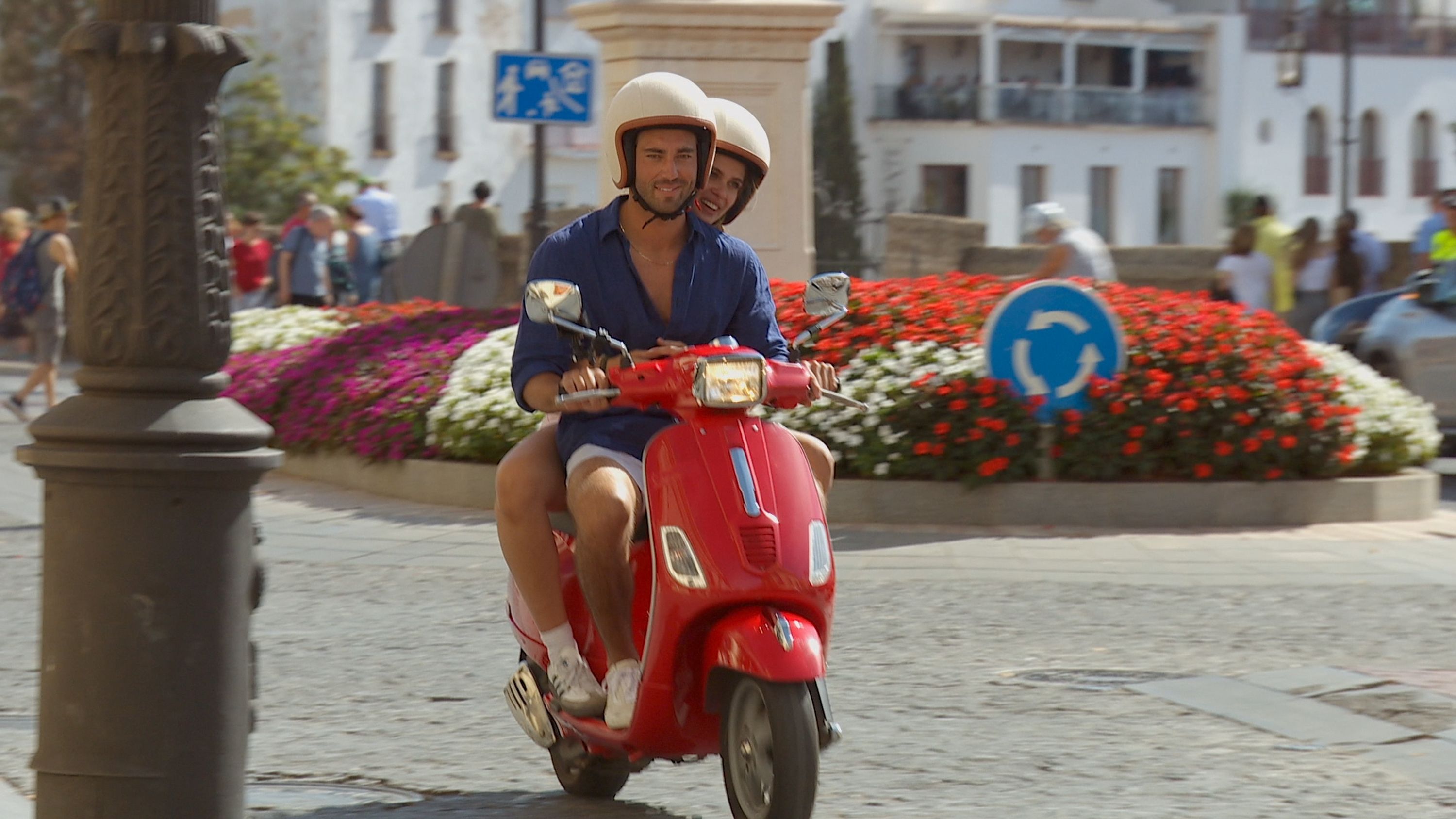Photo shows Joey and Kelsey wearing helmets and riding a red motor scooter.