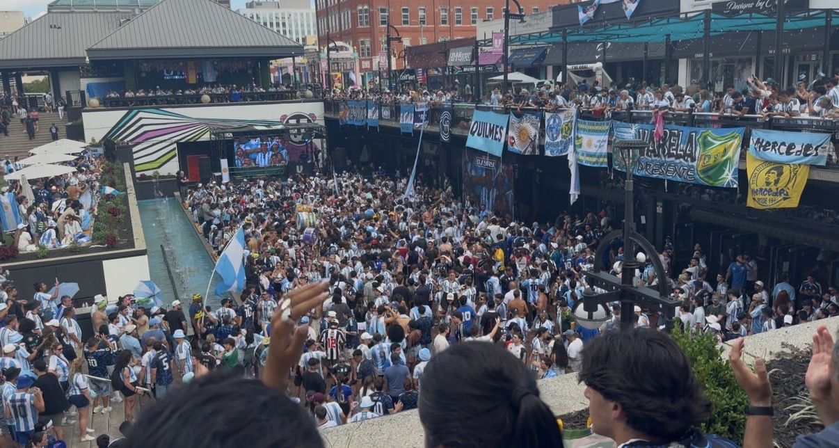 A photo of a large crowd of people wearing white and light blue jerseys gathered in a large outdoor urban area with crowds lining a railing looking at the festivities below.