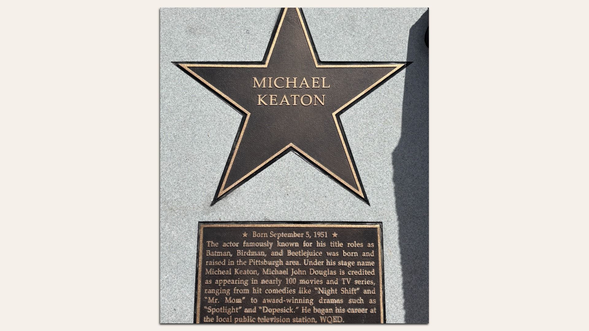 Bronze star and plaque honoring Michael Keaton on a gray stone surface, detailing his birthdate and notable acting roles like "Batman" and "Beetlejuice". His name is misspelled "Micheal" in one sentence. 