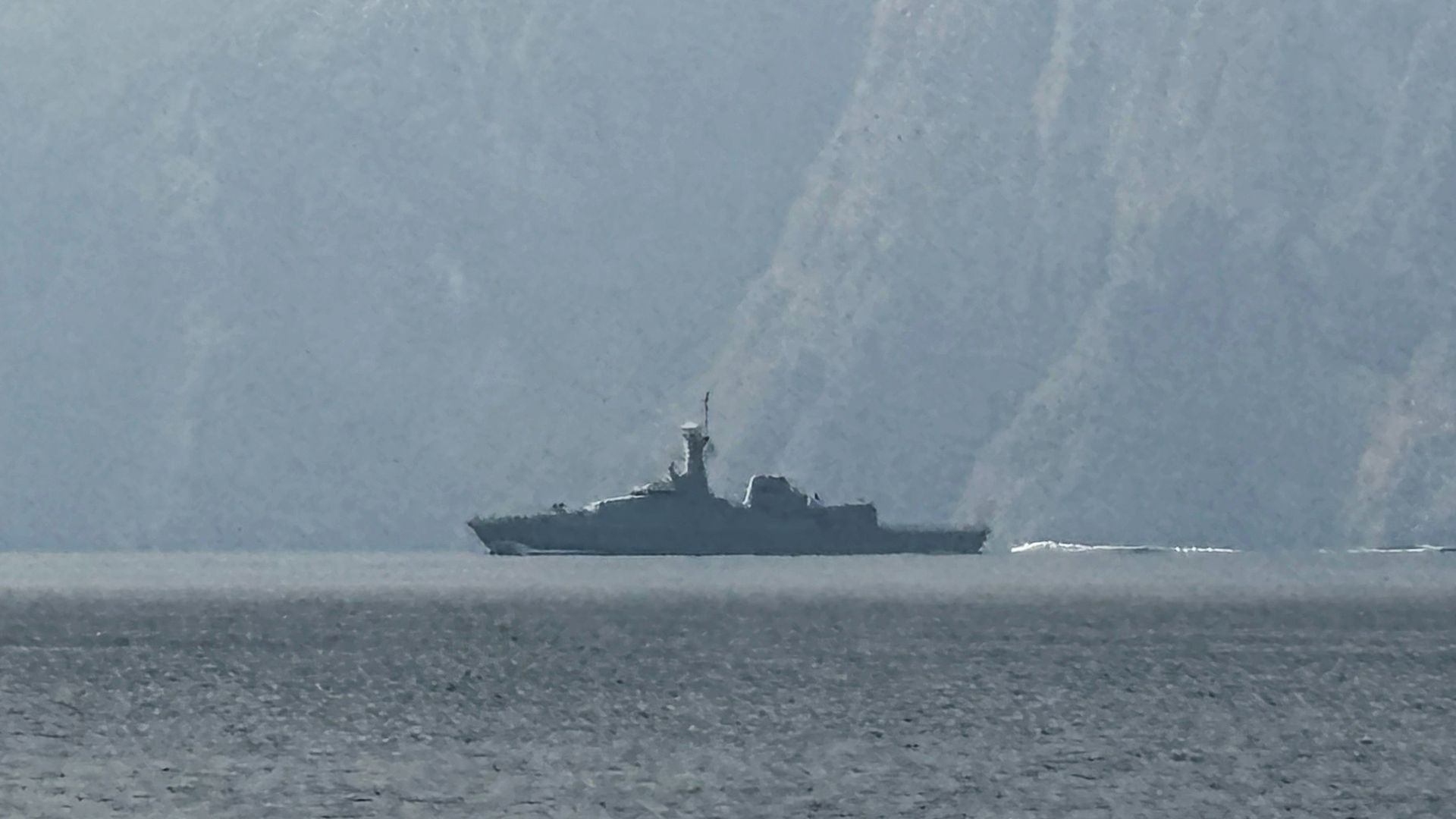 A naval vessel in a waterway with a mountain behind. 