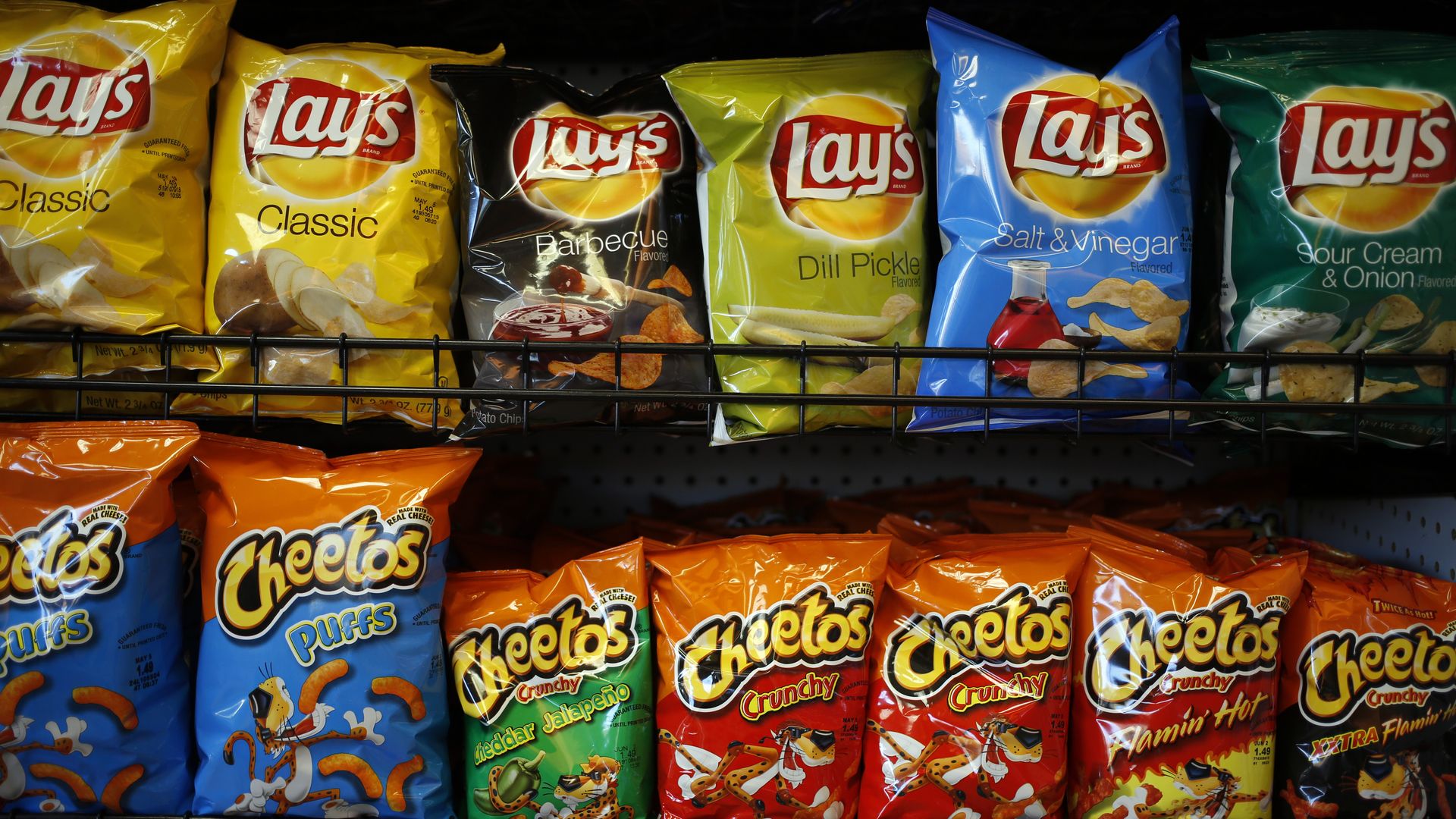 Store shelf loaded with Layβs chip bags in flavors like Classic, Barbecue, Dill Pickle, Salt & Vinegar, and Sour Cream & Onion; bottom row shows orange Cheetos bags.