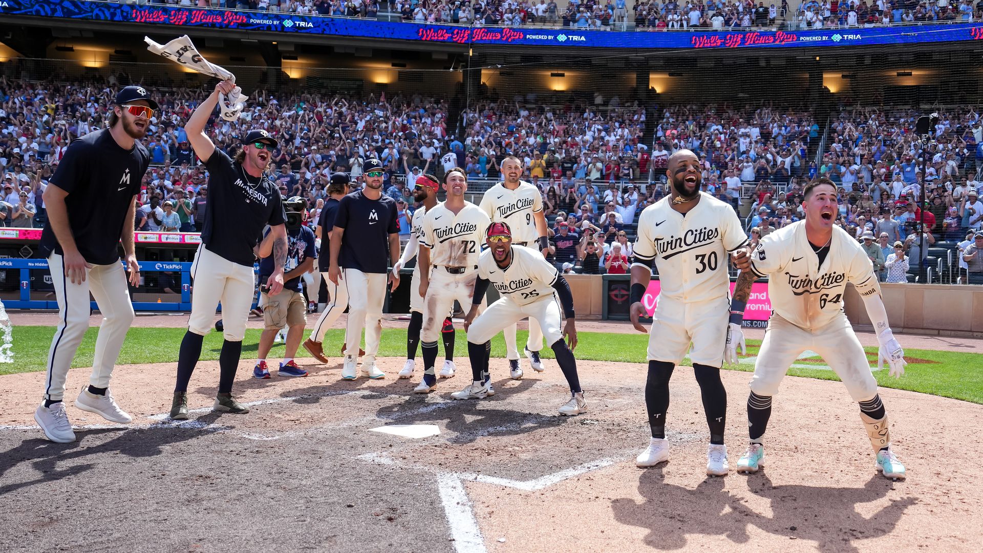Twins players stand around home plate cheering 