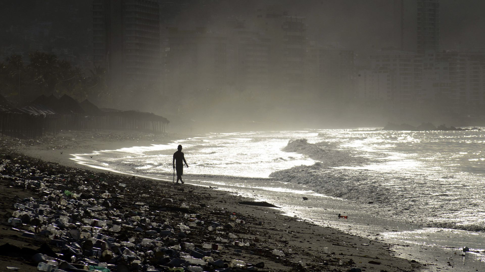 Black and white photo of a person walking on the edge of Santa Lucia beach in Mexico filled with plastic bottles everywhere