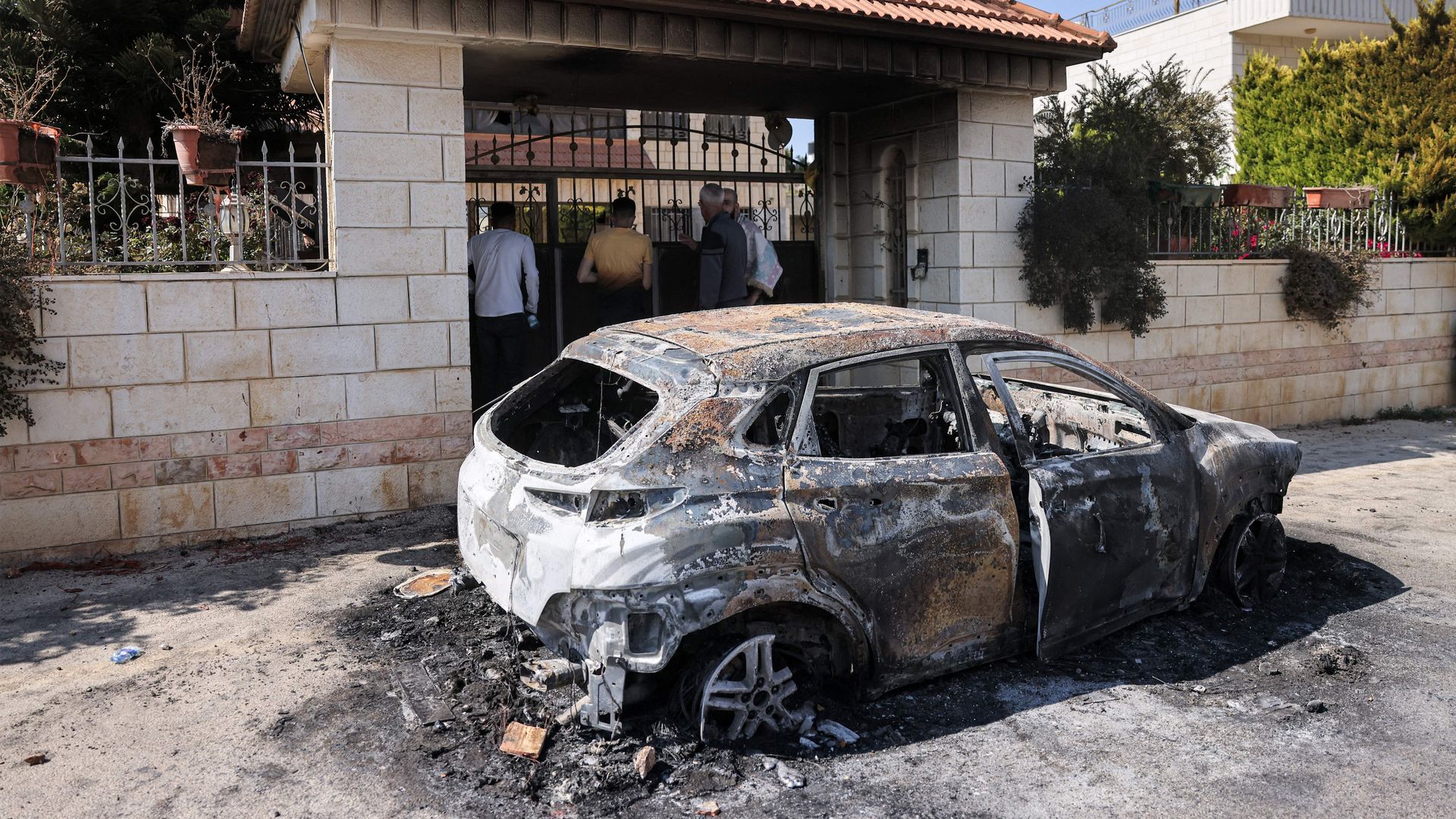 People stand by a torched vehicle, reportedly set ablaze by Israeli settlers, in the village of Turmus Aya near the occupied West Bank city of Ramallah on June 21, 2023. 